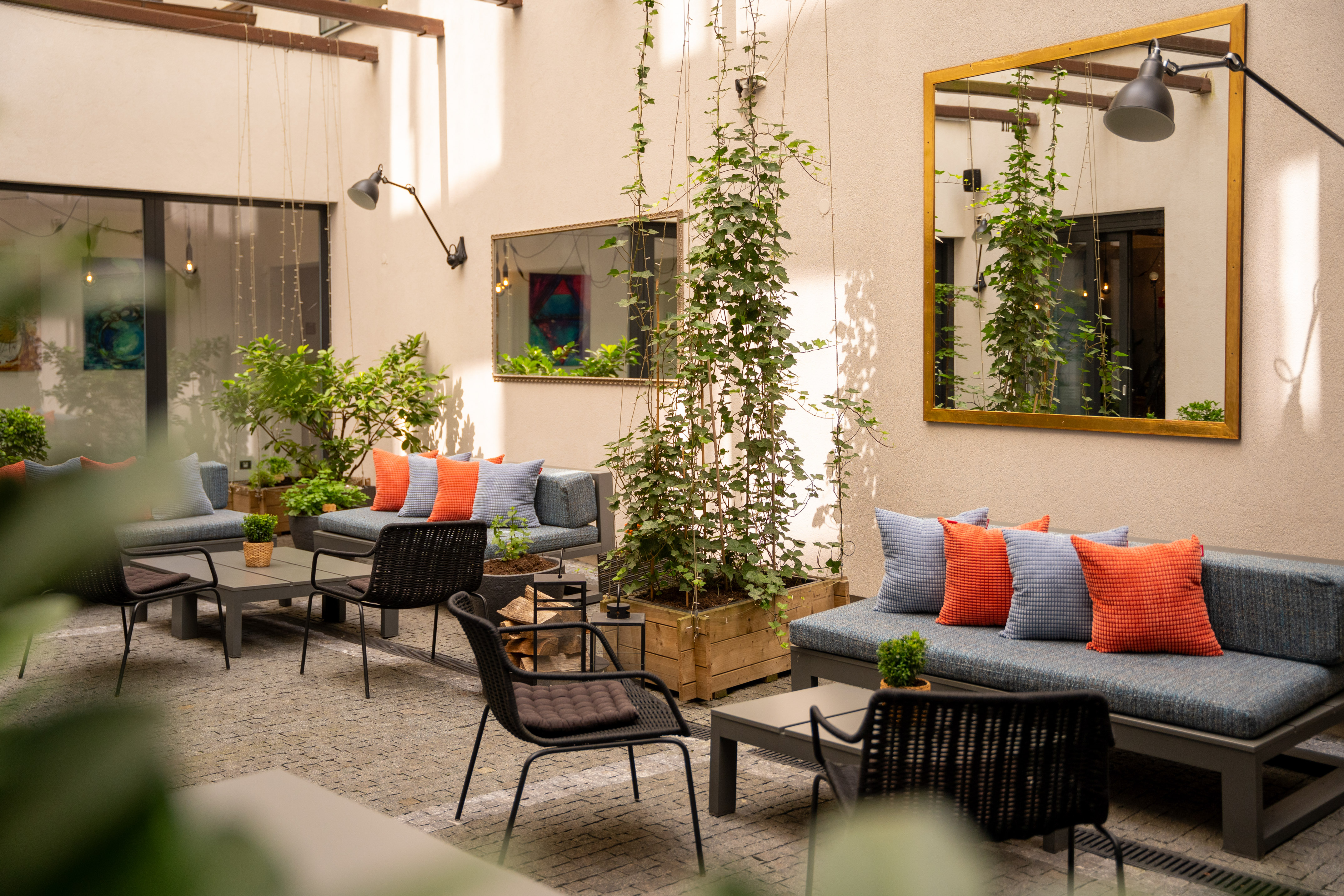 Stylish outdoor lounge area with comfortable seating, greenery, and wall mirrors.