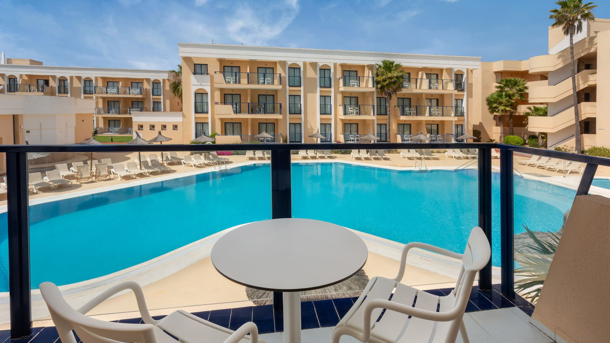 Balcony view of hotel resort pool with sun loungers and palm trees.