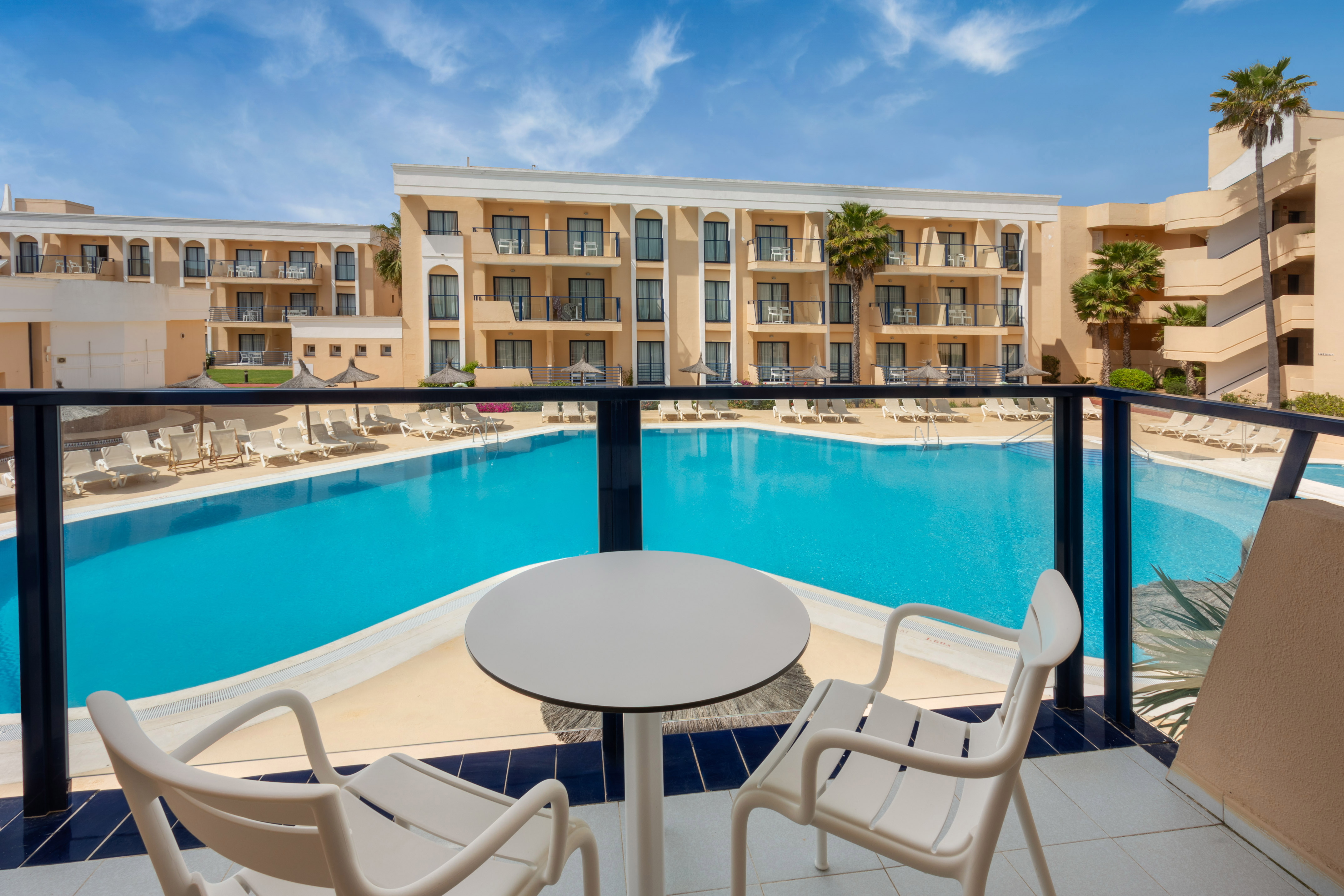Balcony view of hotel resort pool with sun loungers and palm trees.