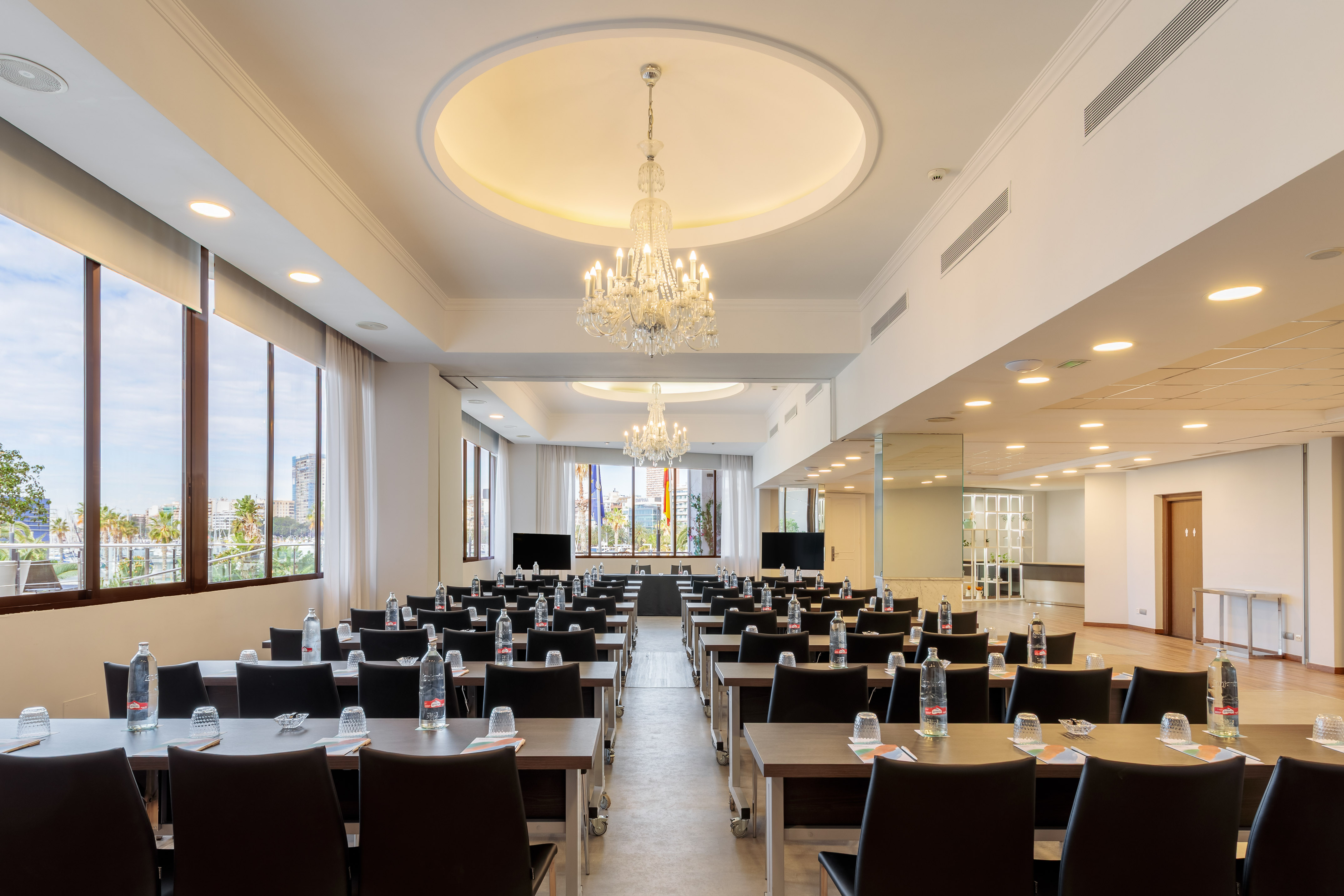 Modern conference room with classroom setup, large windows, and chandeliers.