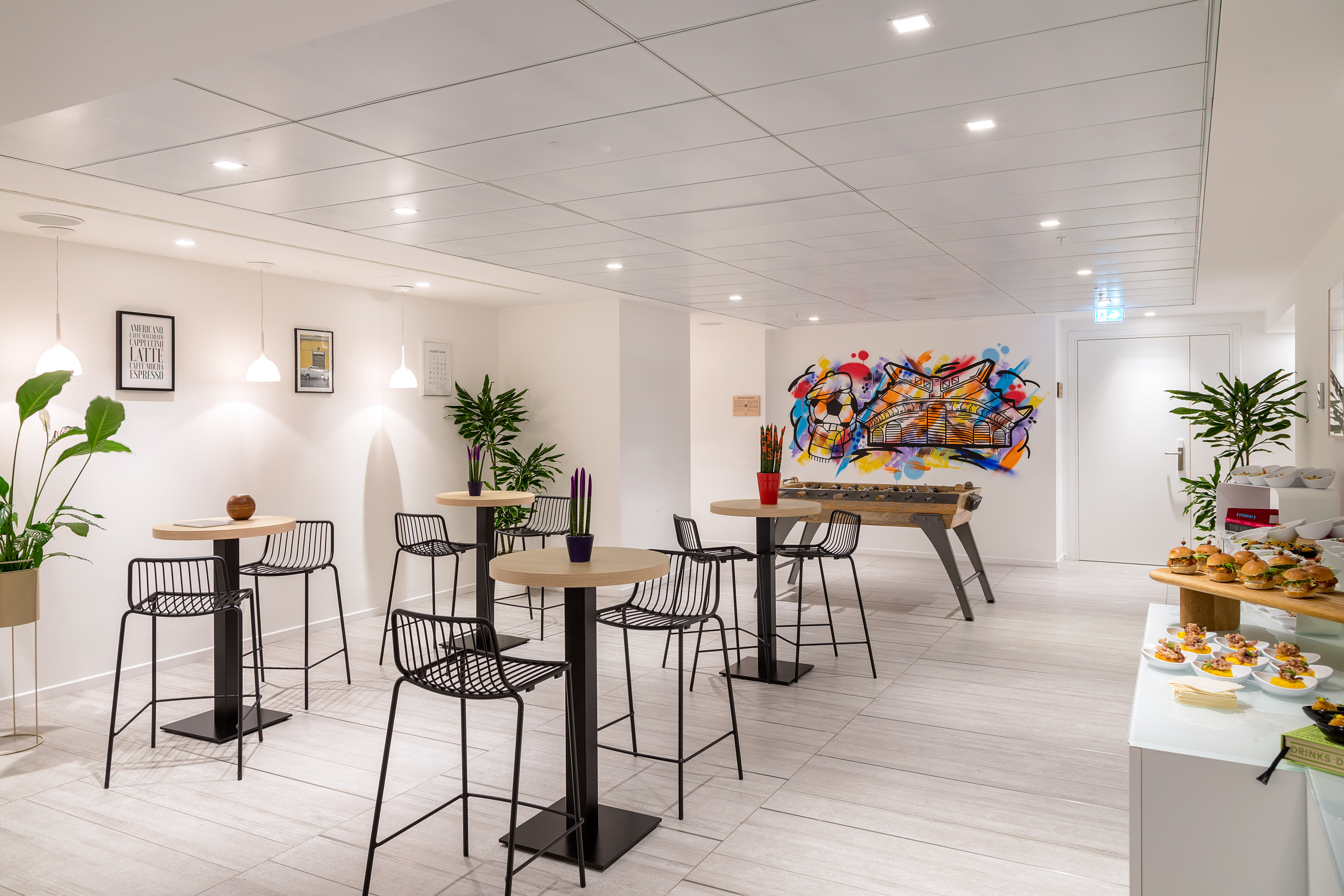 Modern break room: high tables, bar stools, vibrant graffiti, foosball, and catering.