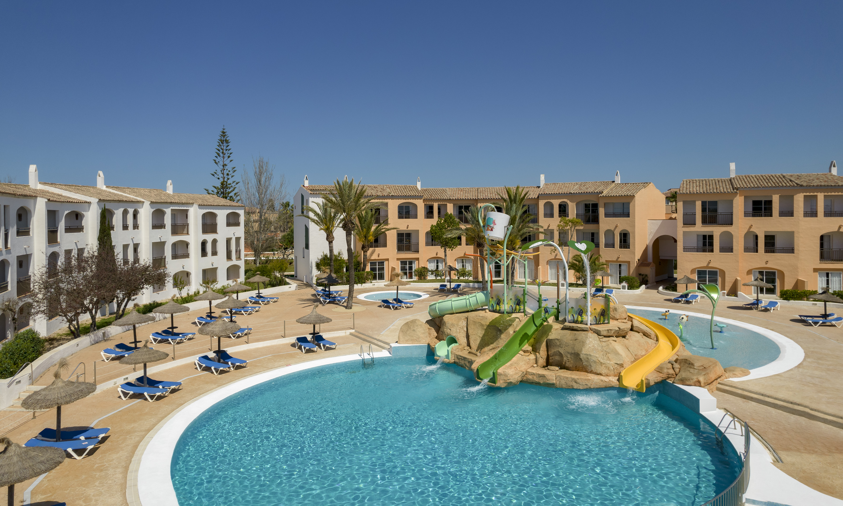 Sunny Mediterranean resort with large pool, kids' water park, and hotel.