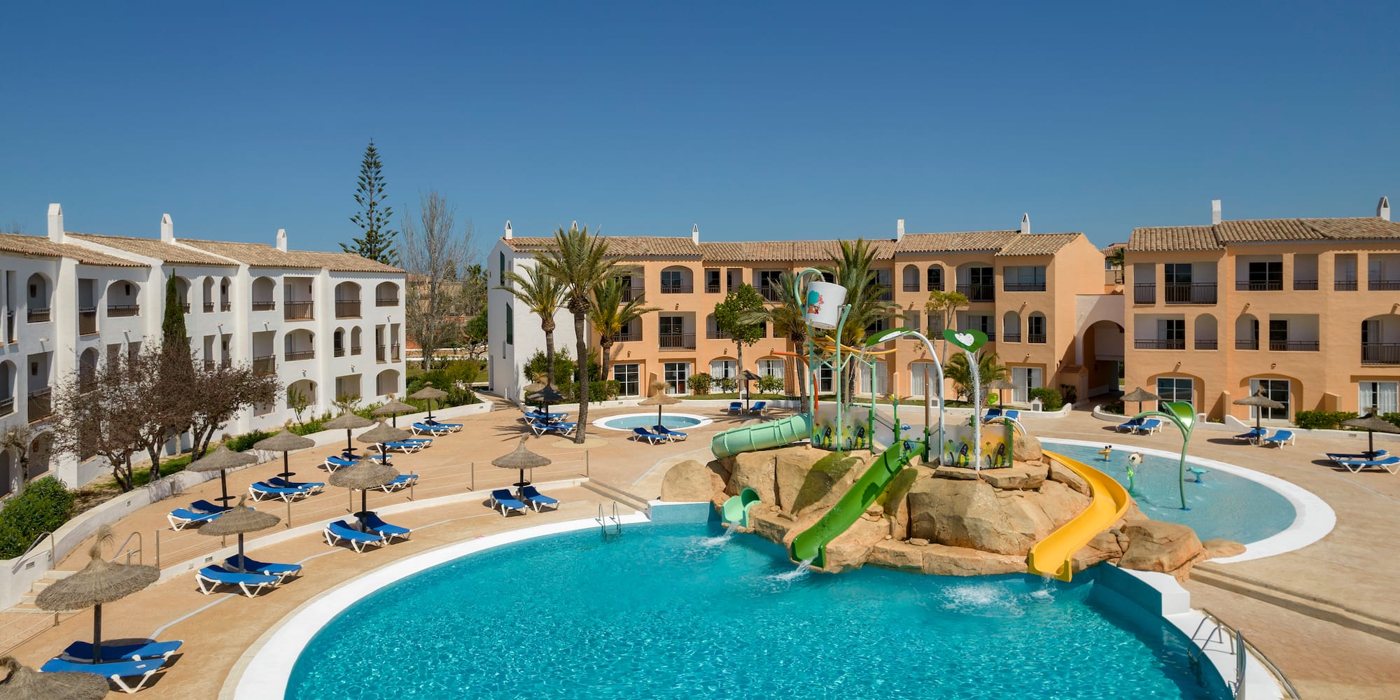 Sunny Mediterranean resort with large pool, kids' water park, and hotel.