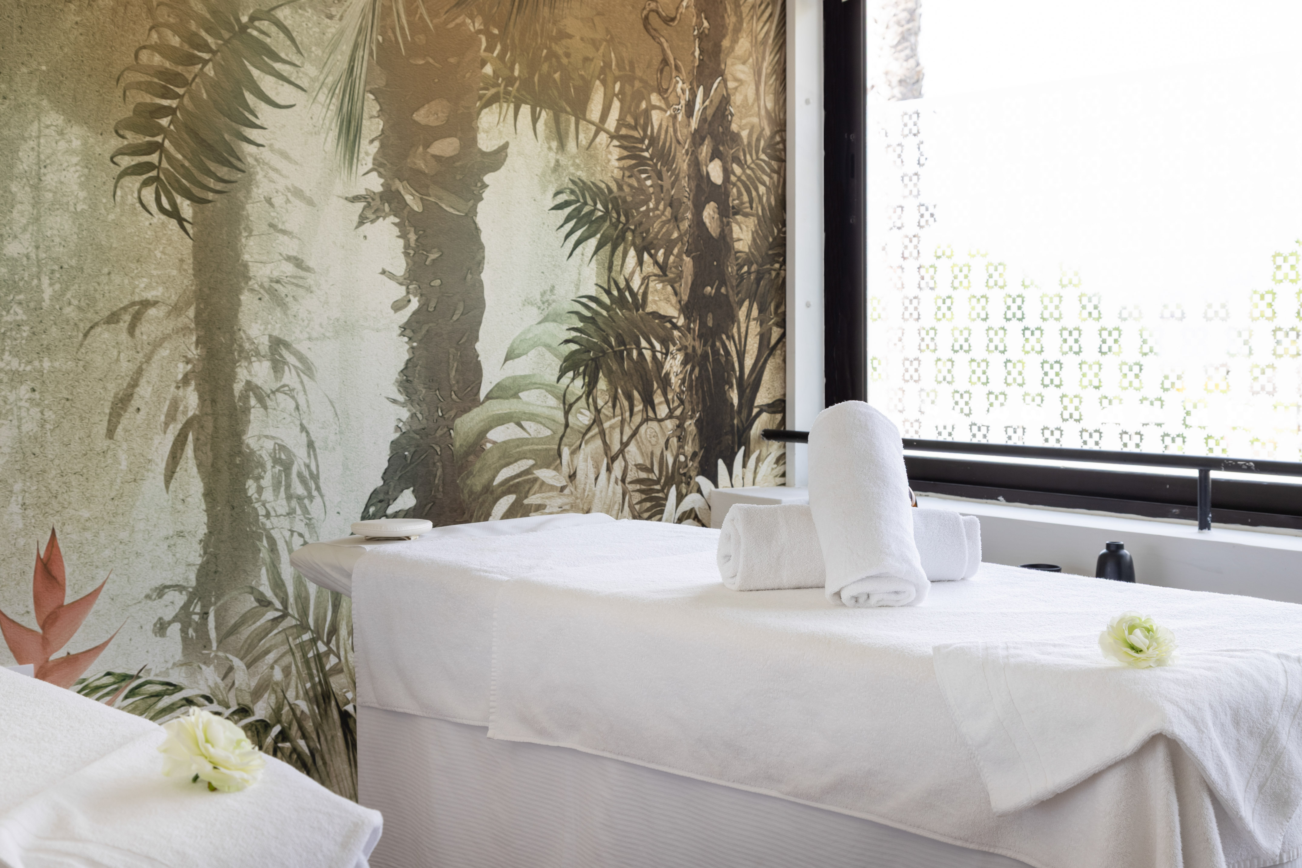 Relaxing spa room with tropical jungle mural, white massage beds, clean towels.