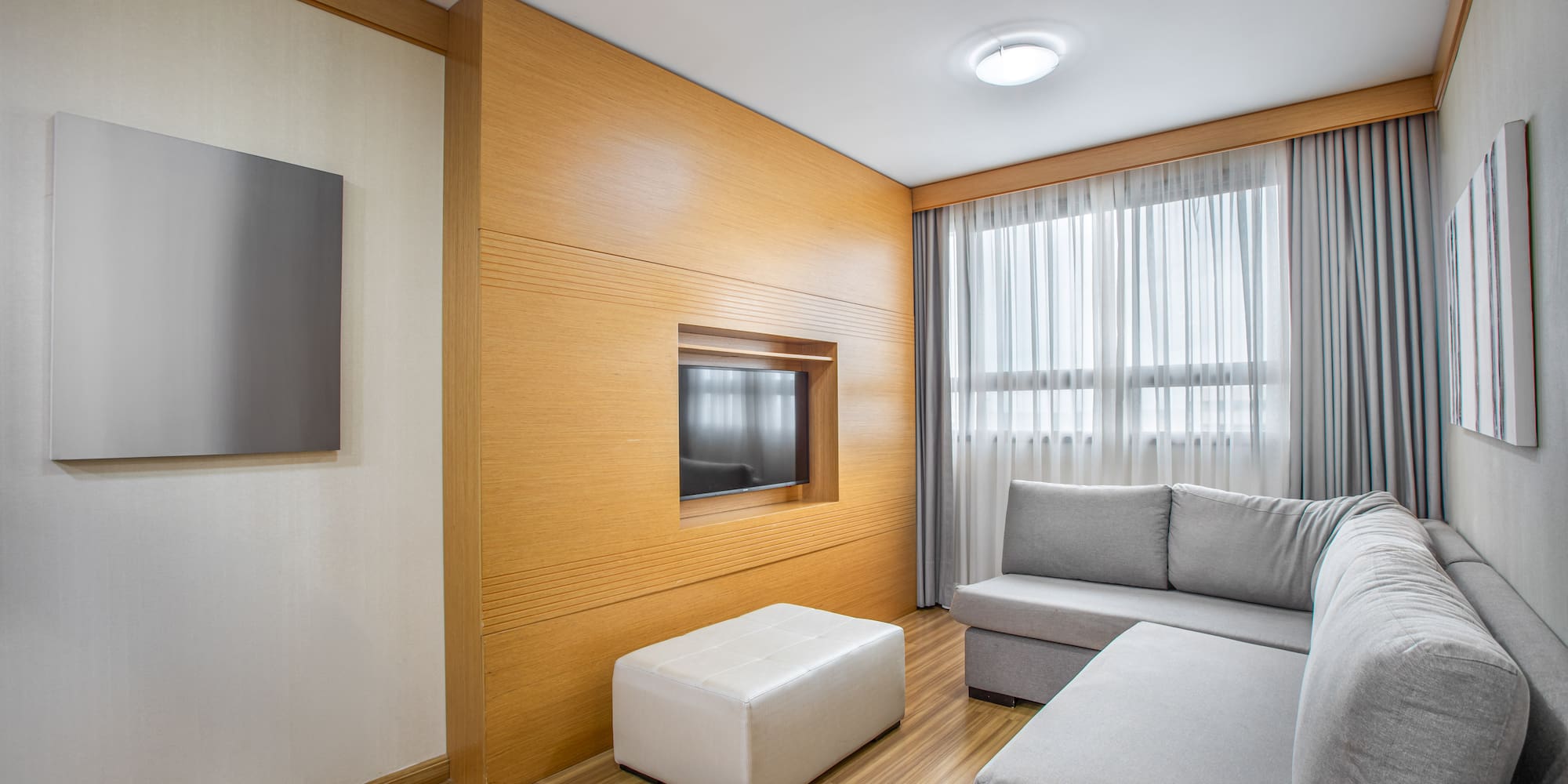 Modern living room with gray sofa, wood panel TV wall, and bright window.