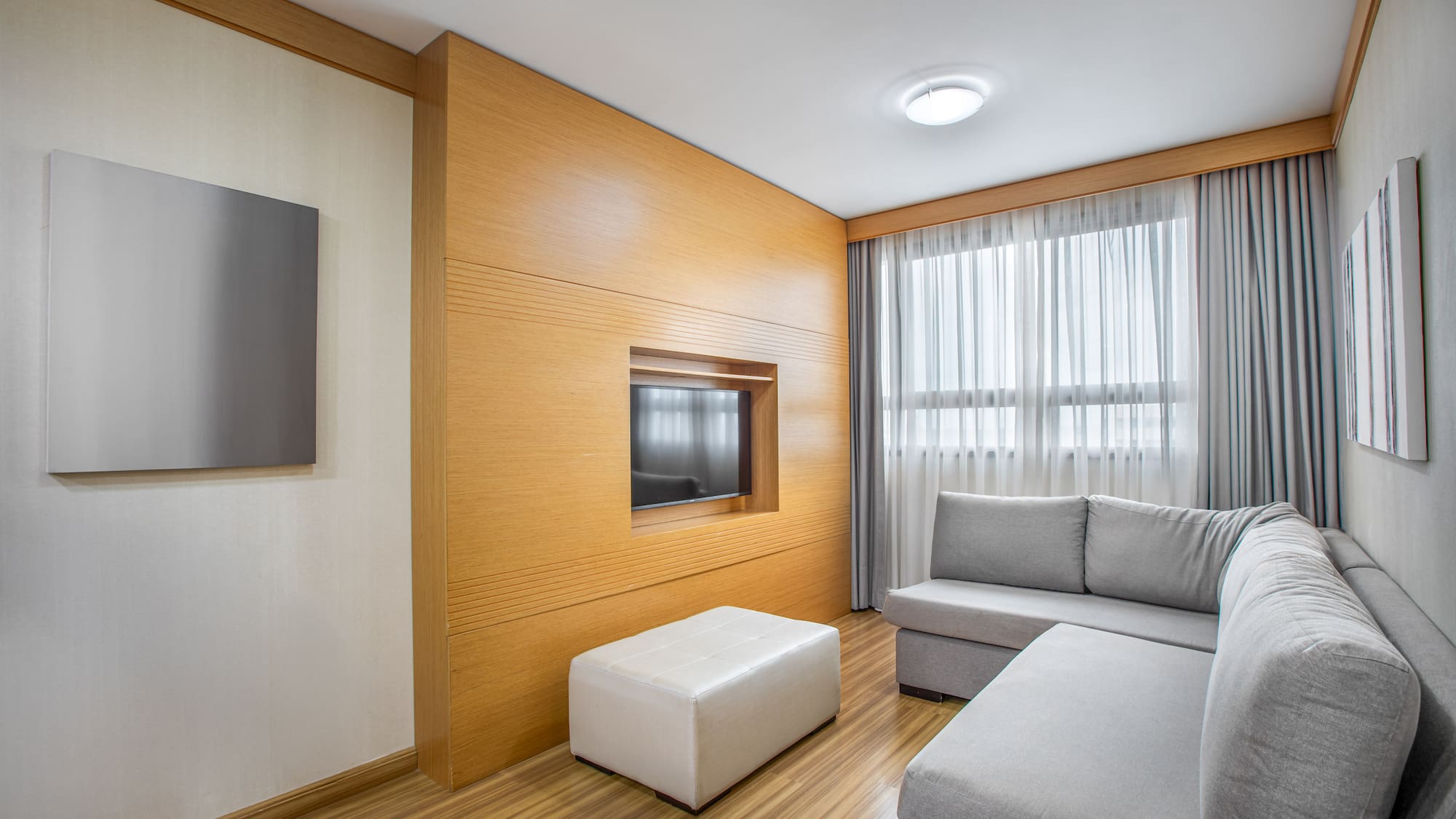 Modern living room with gray sofa, wood panel TV wall, and bright window.