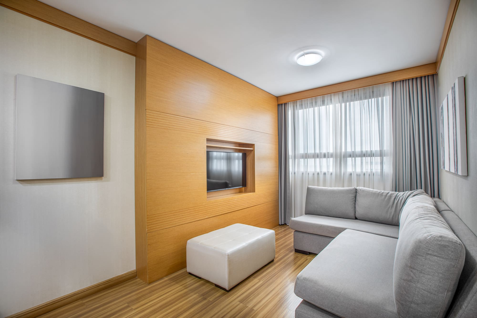 Modern living room with gray sofa, wood panel TV wall, and bright window.