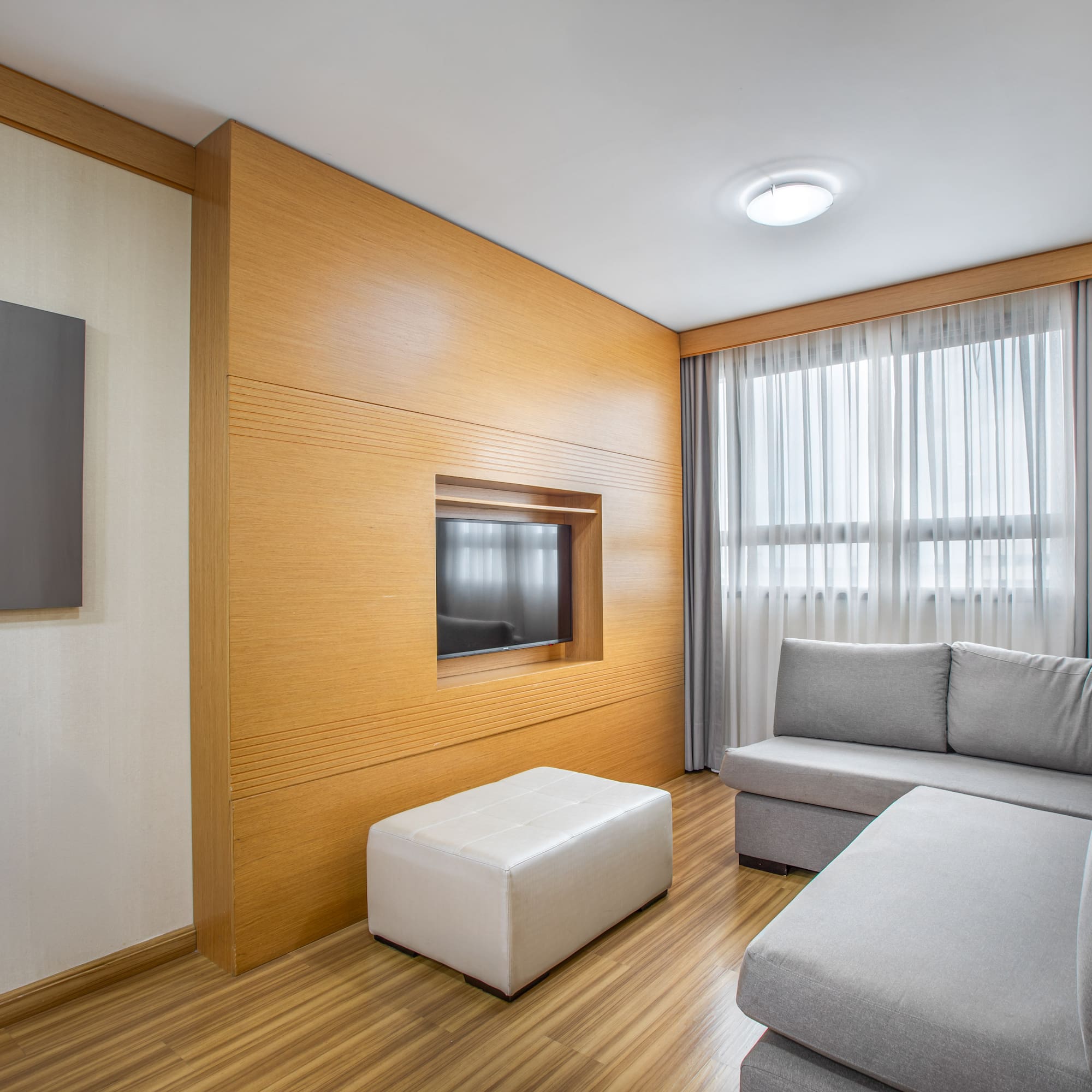 Modern living room with gray sofa, wood panel TV wall, and bright window.