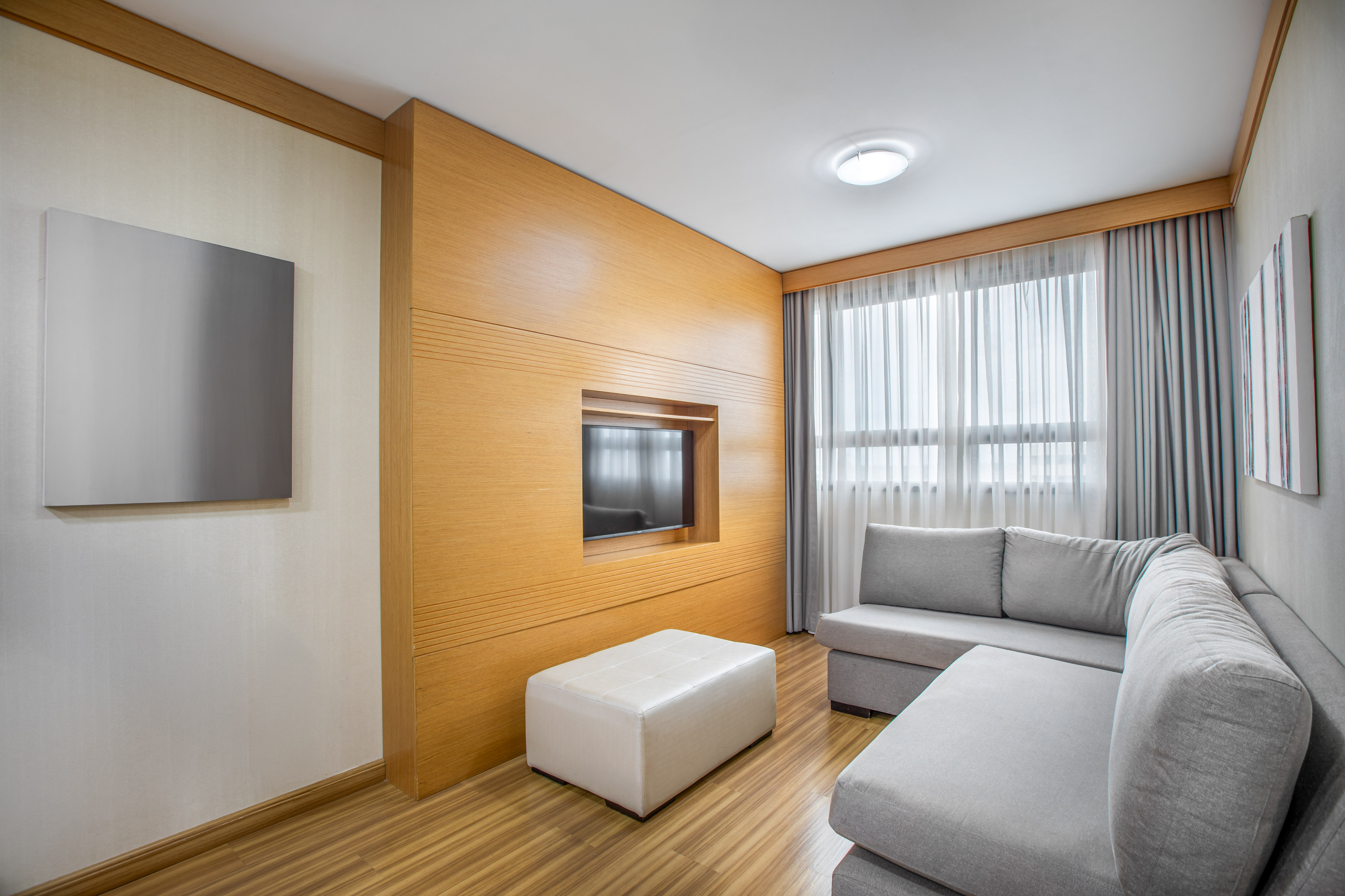 Modern living room with gray sofa, wood panel TV wall, and bright window.