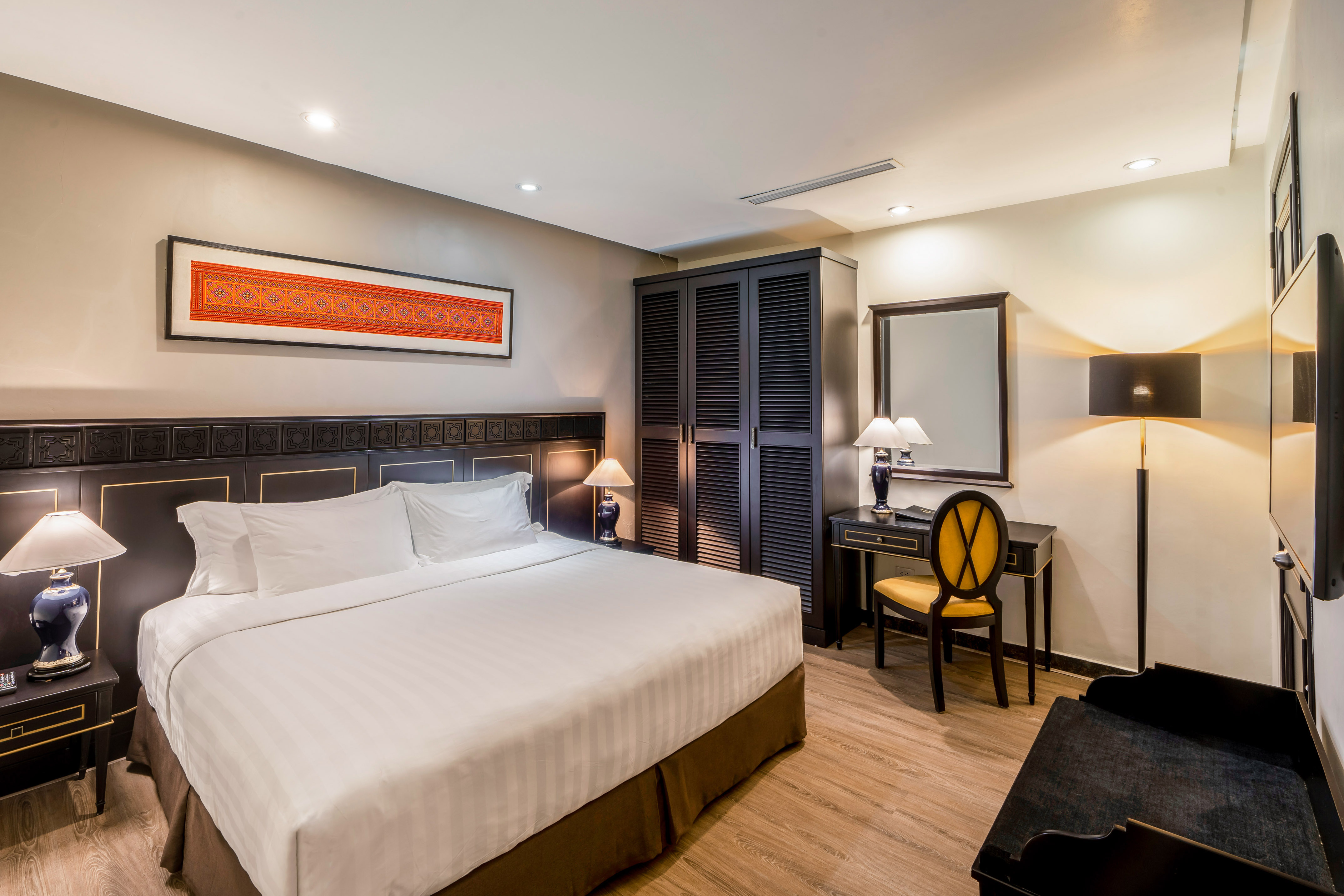 Hotel bedroom with comfortable bed, dark wood furniture, and vibrant art.
