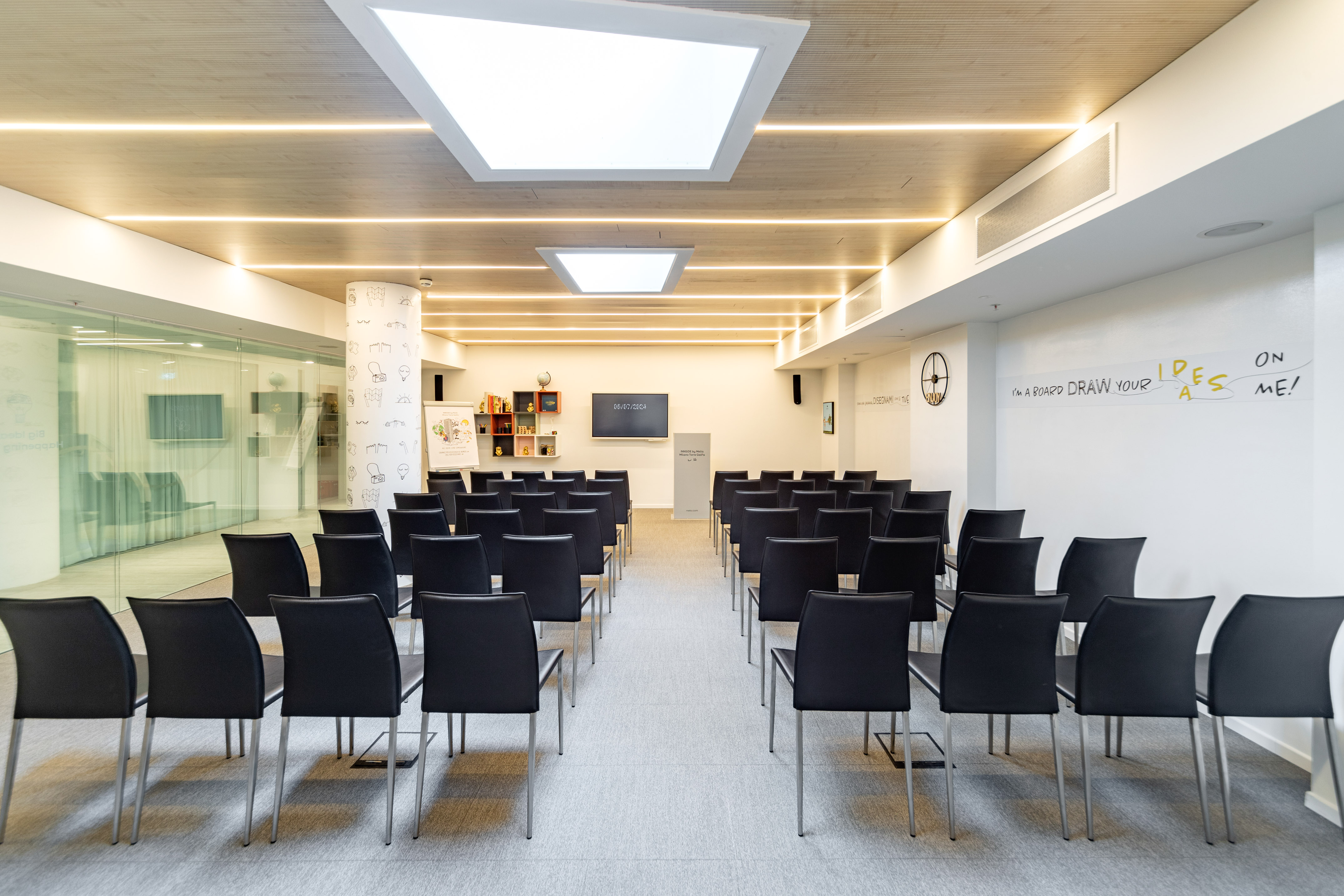 Modern meeting room with black chairs, screen, podium, and wooden ceiling.