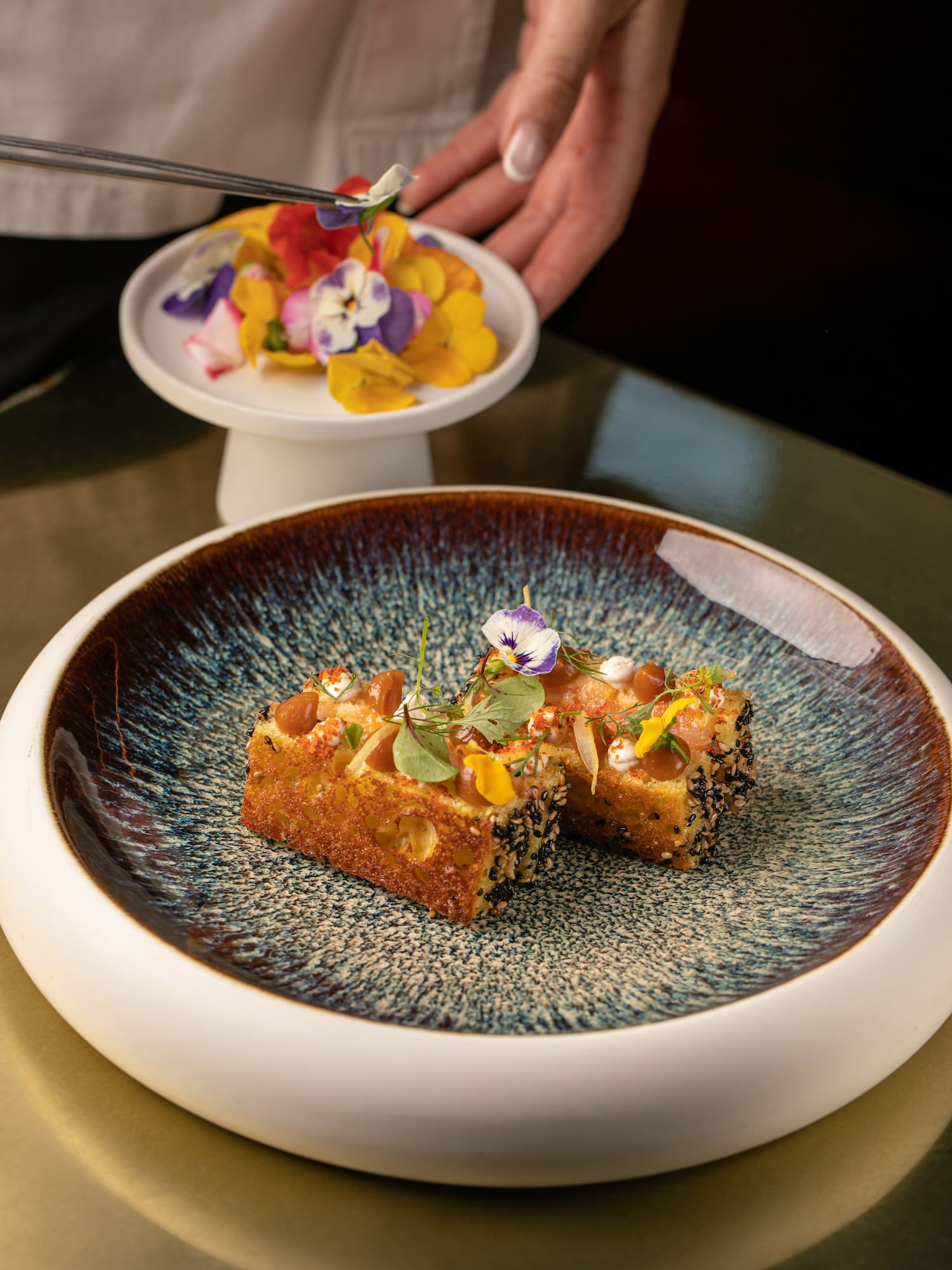 Chef garnishes gourmet sesame toast with colorful edible flowers.