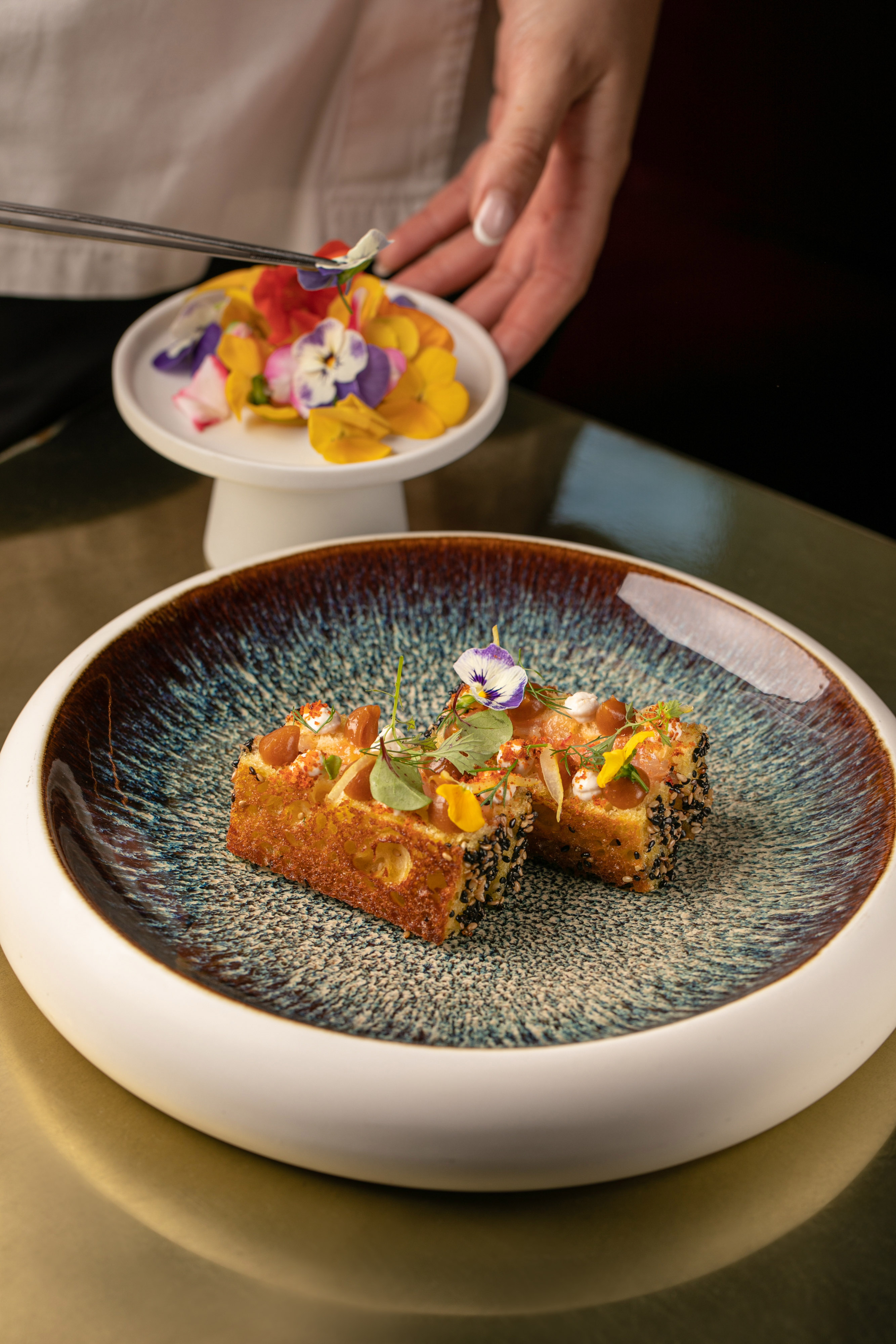 Chef garnishes gourmet sesame toast with colorful edible flowers.