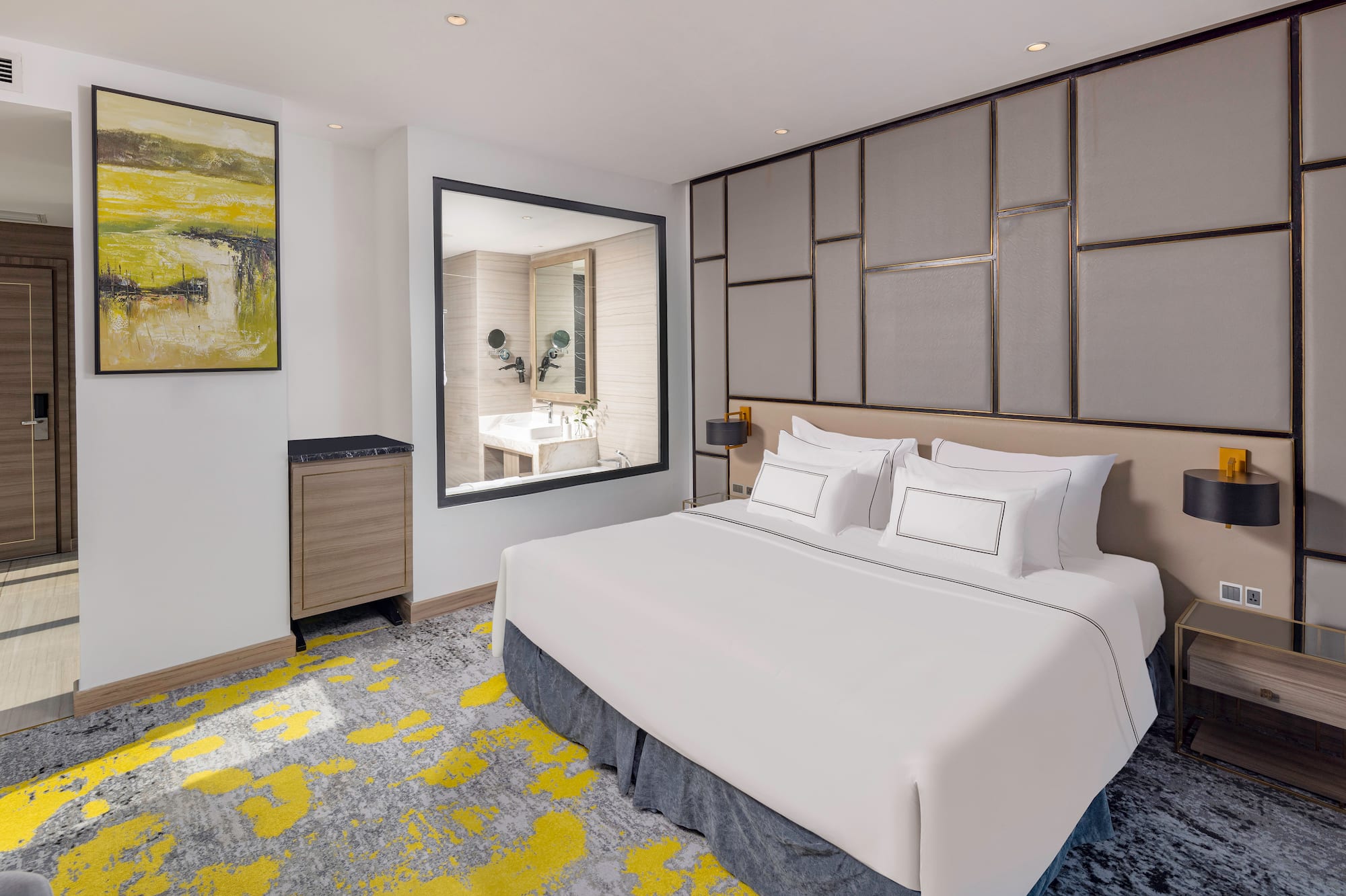 Modern hotel room with king bed, abstract yellow/grey carpet, and bathroom window.