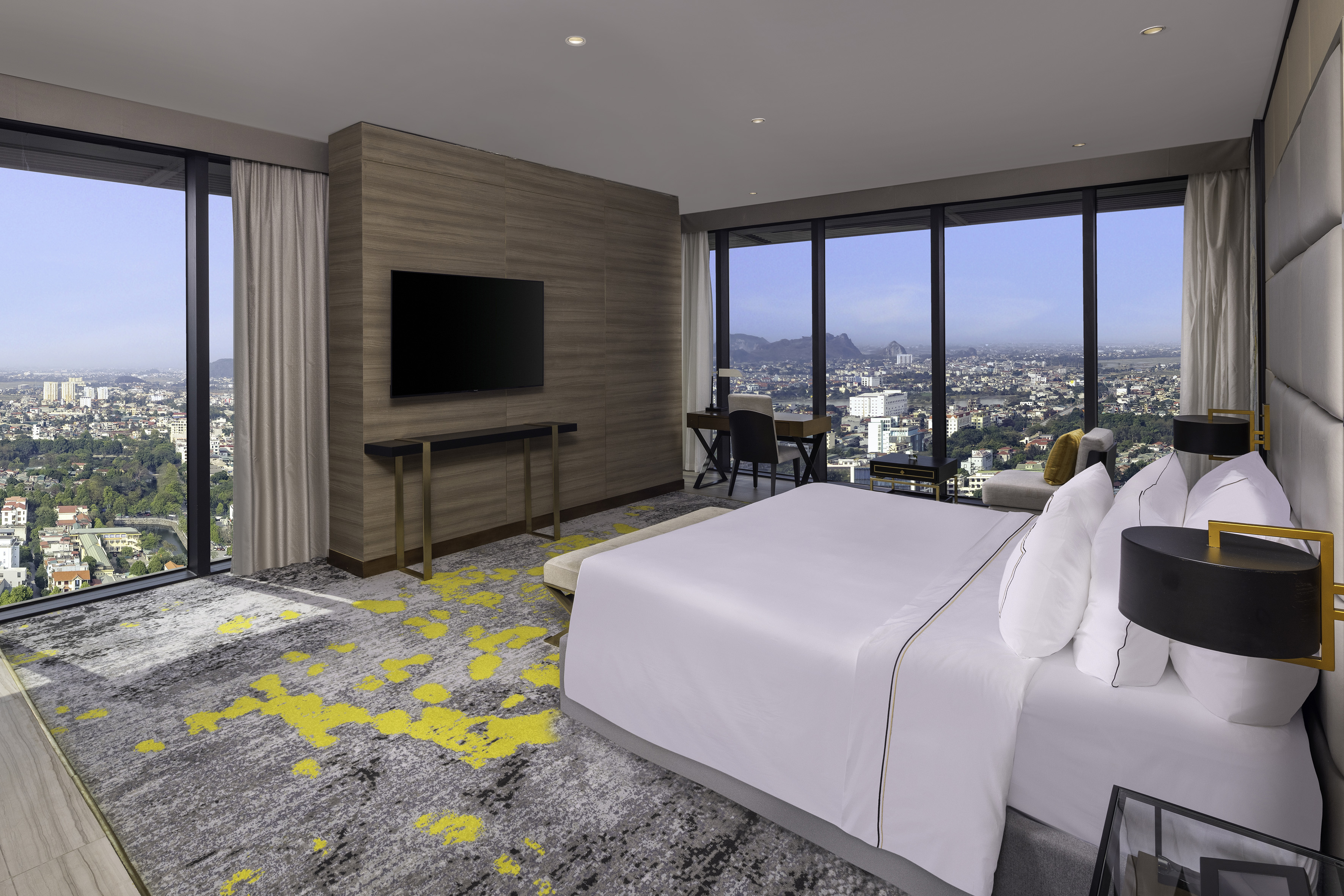 Modern hotel room with panoramic city view, king bed, and work desk.