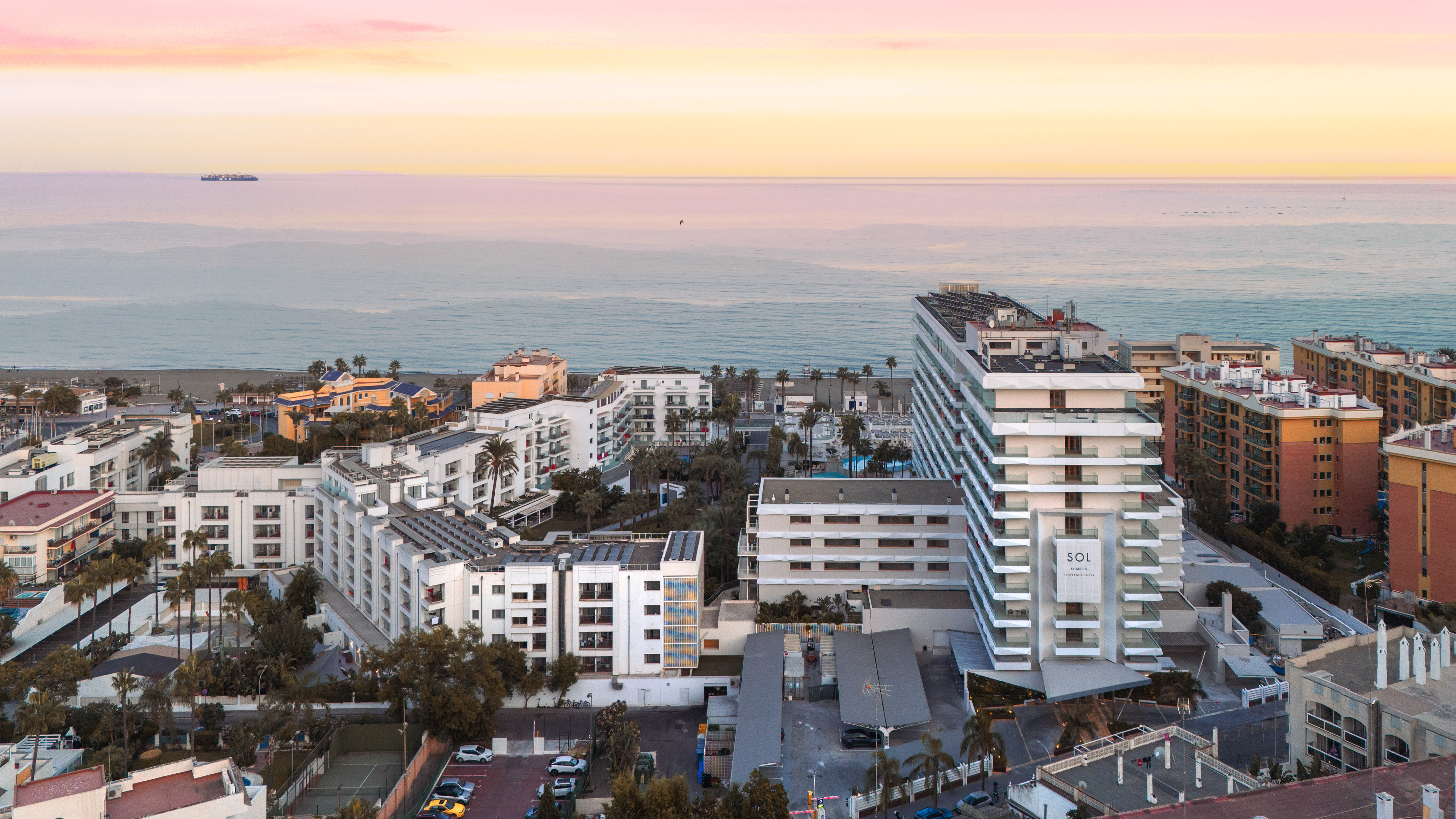 Oceanfront city with modern buildings, beach, and colorful sunset sky.