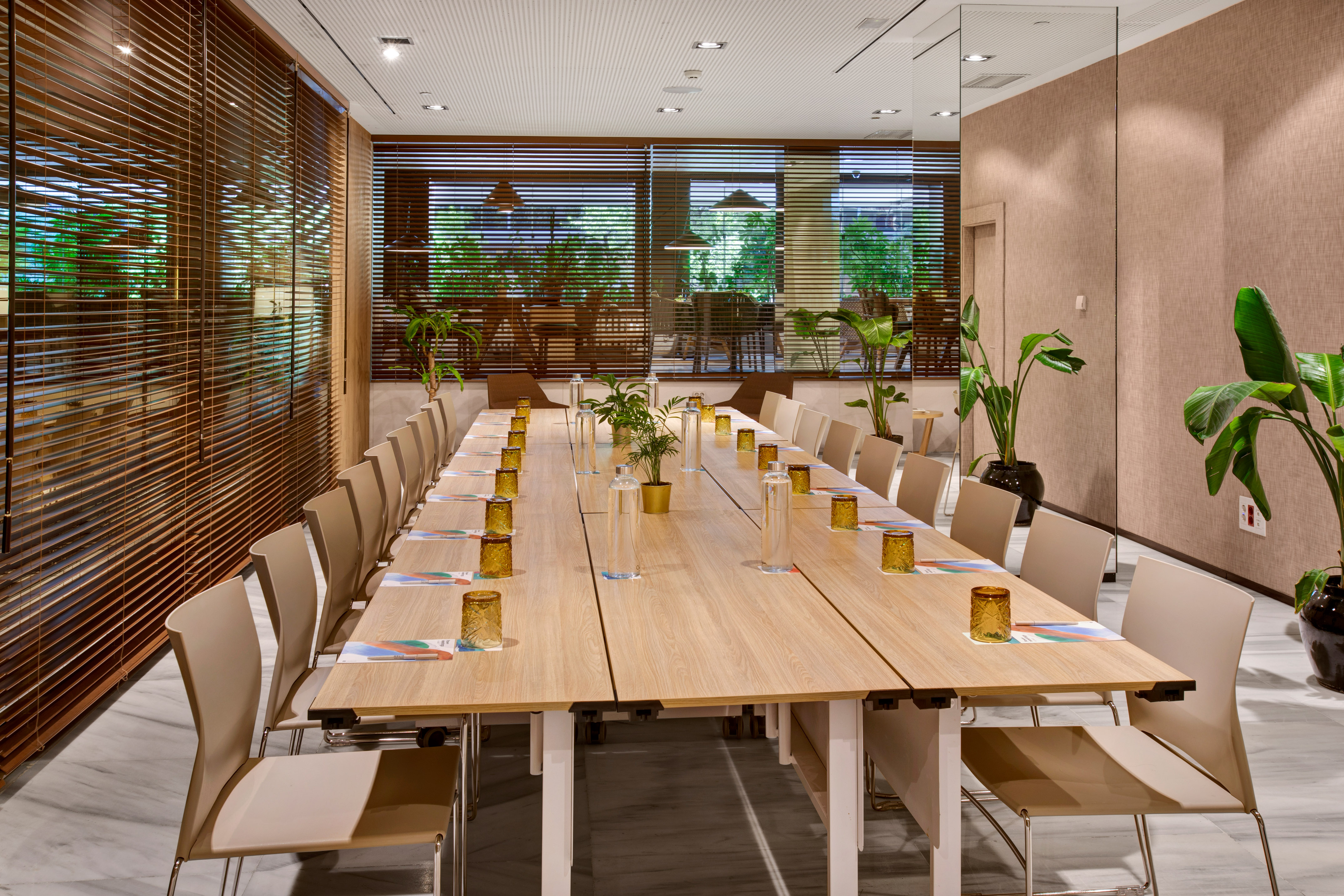 Modern meeting room with large wooden table, beige chairs, and green plants.