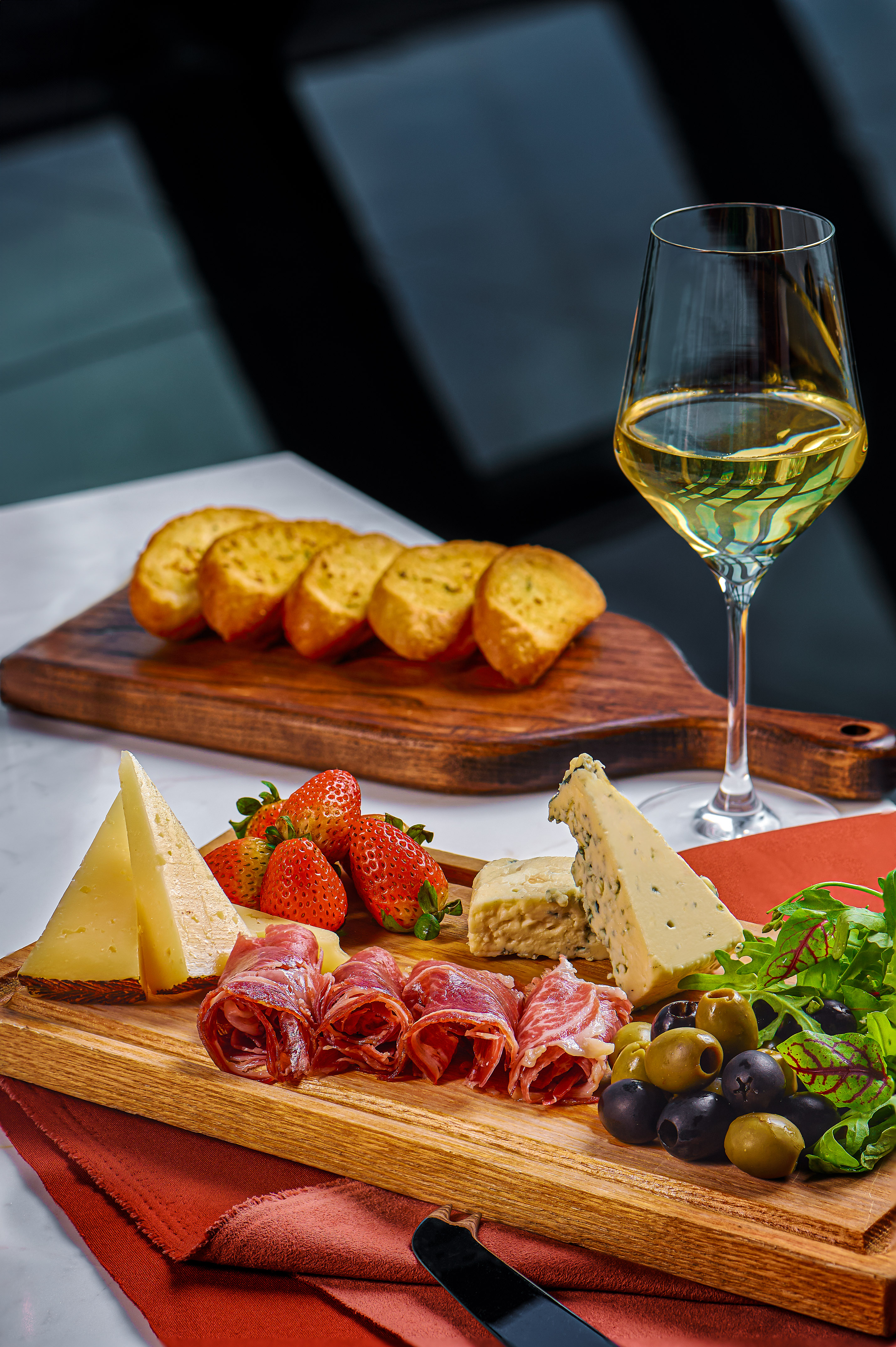 Cheese and charcuterie board with white wine, strawberries, olives, toasted bread.
