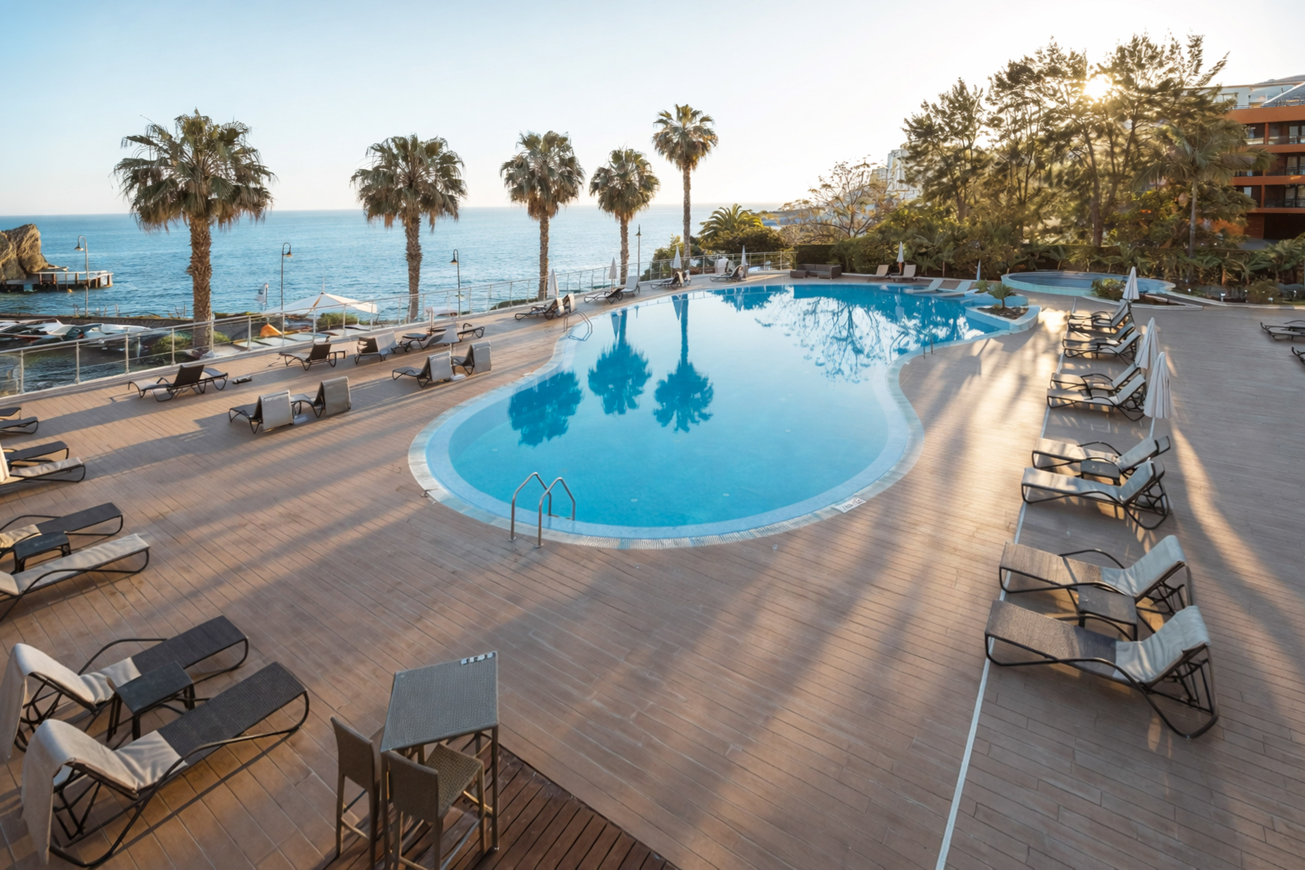 a pool with chairs and a deck with a body of water in the background