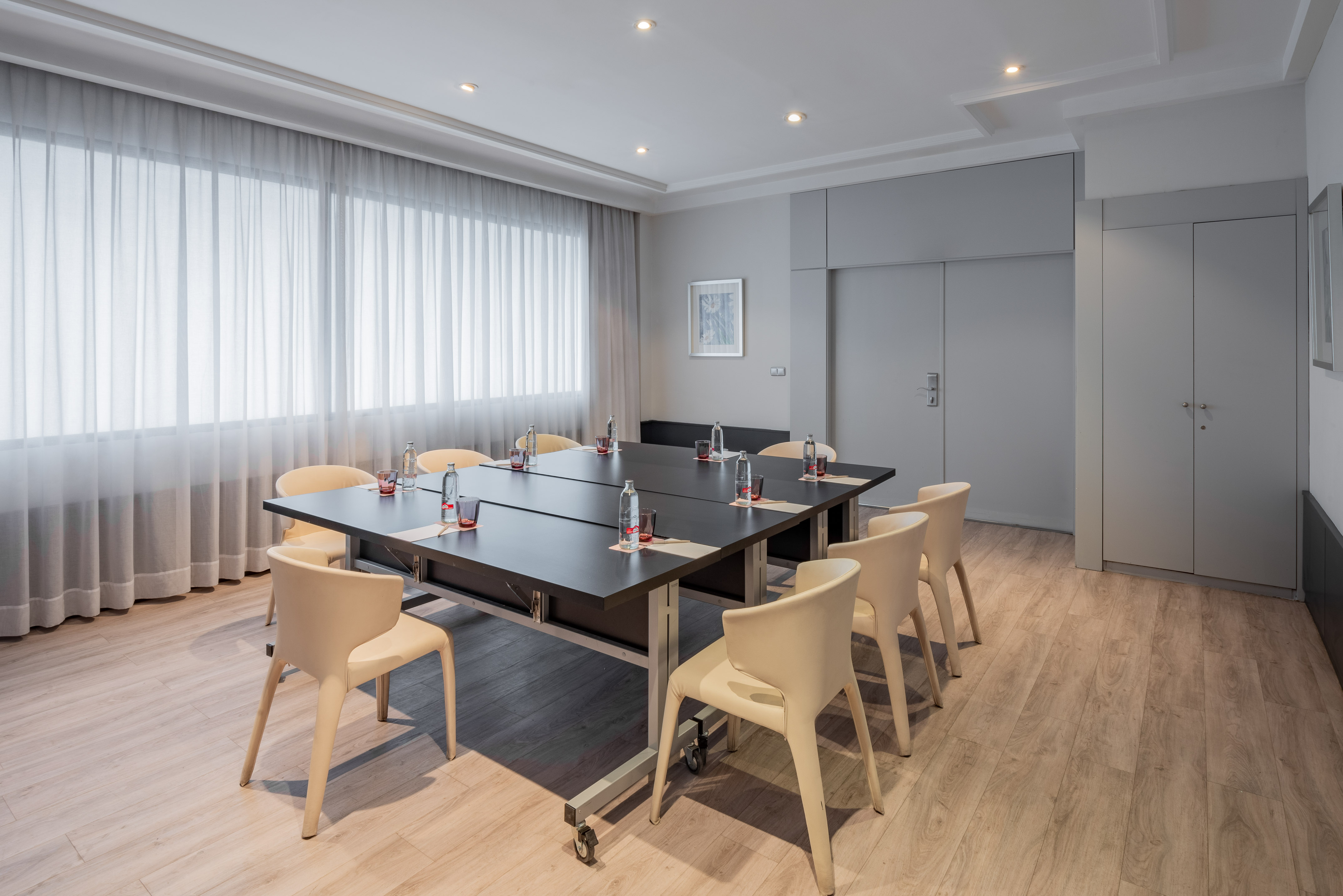 Executive meeting room with black table, cream chairs, wood floor, sheer curtains.