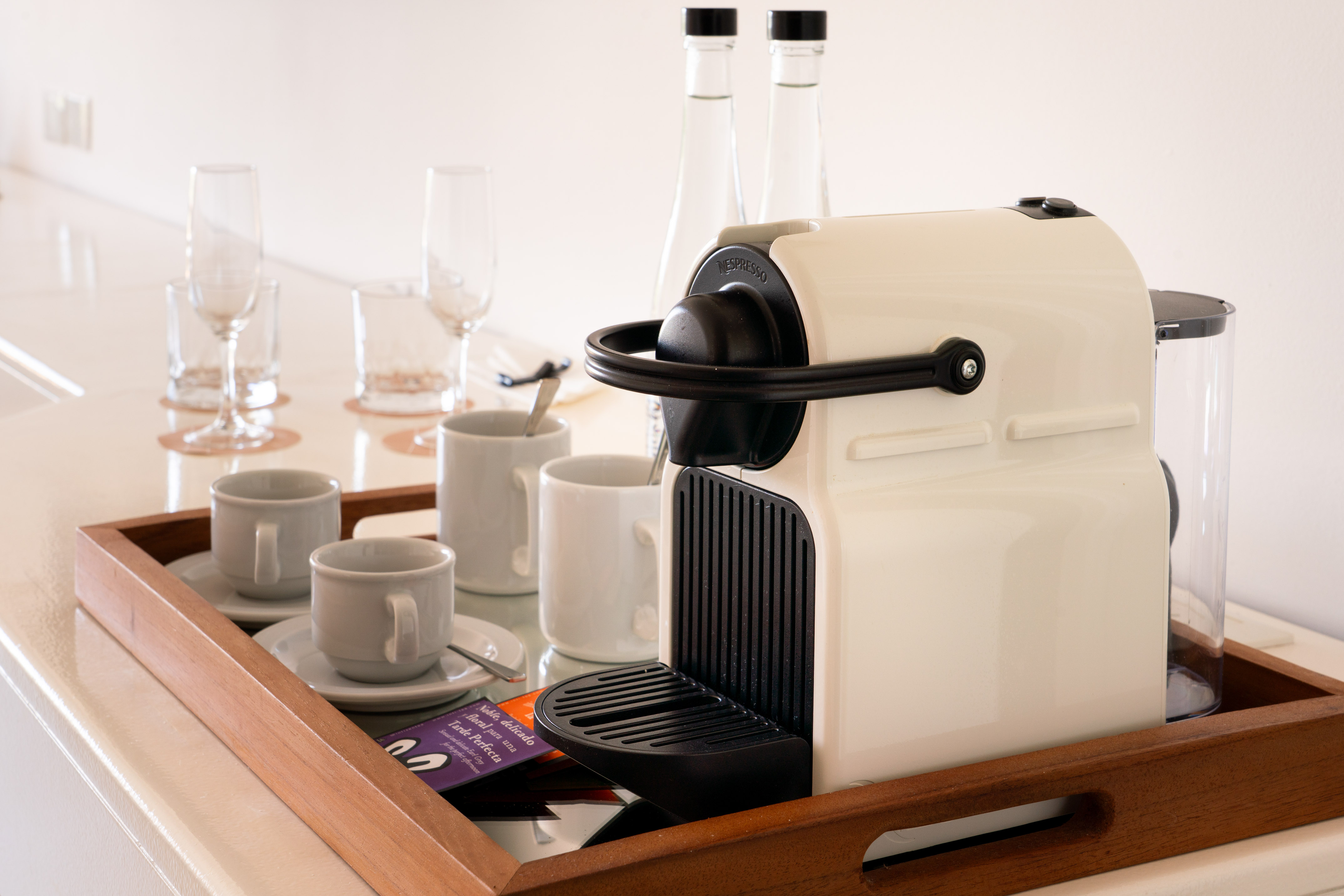 Cream Nespresso coffee machine, cups, and glasses on a hotel beverage tray.