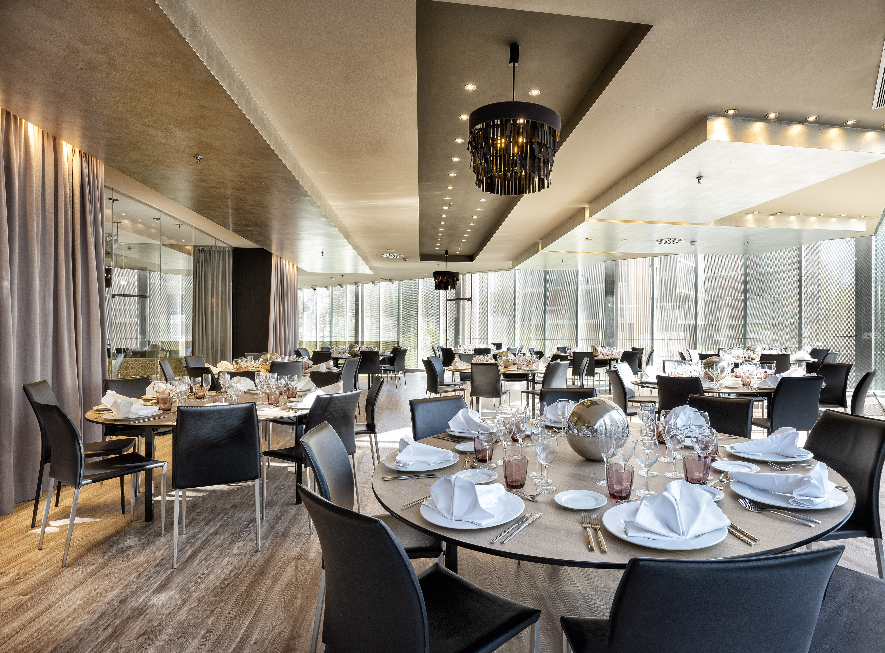 Modern restaurant with elegant round tables, black chairs, and chandelier. - FORUM - فندق برشلونة كوندال مار(Condal Mar) المنتسب لـ Melia, برشلونة