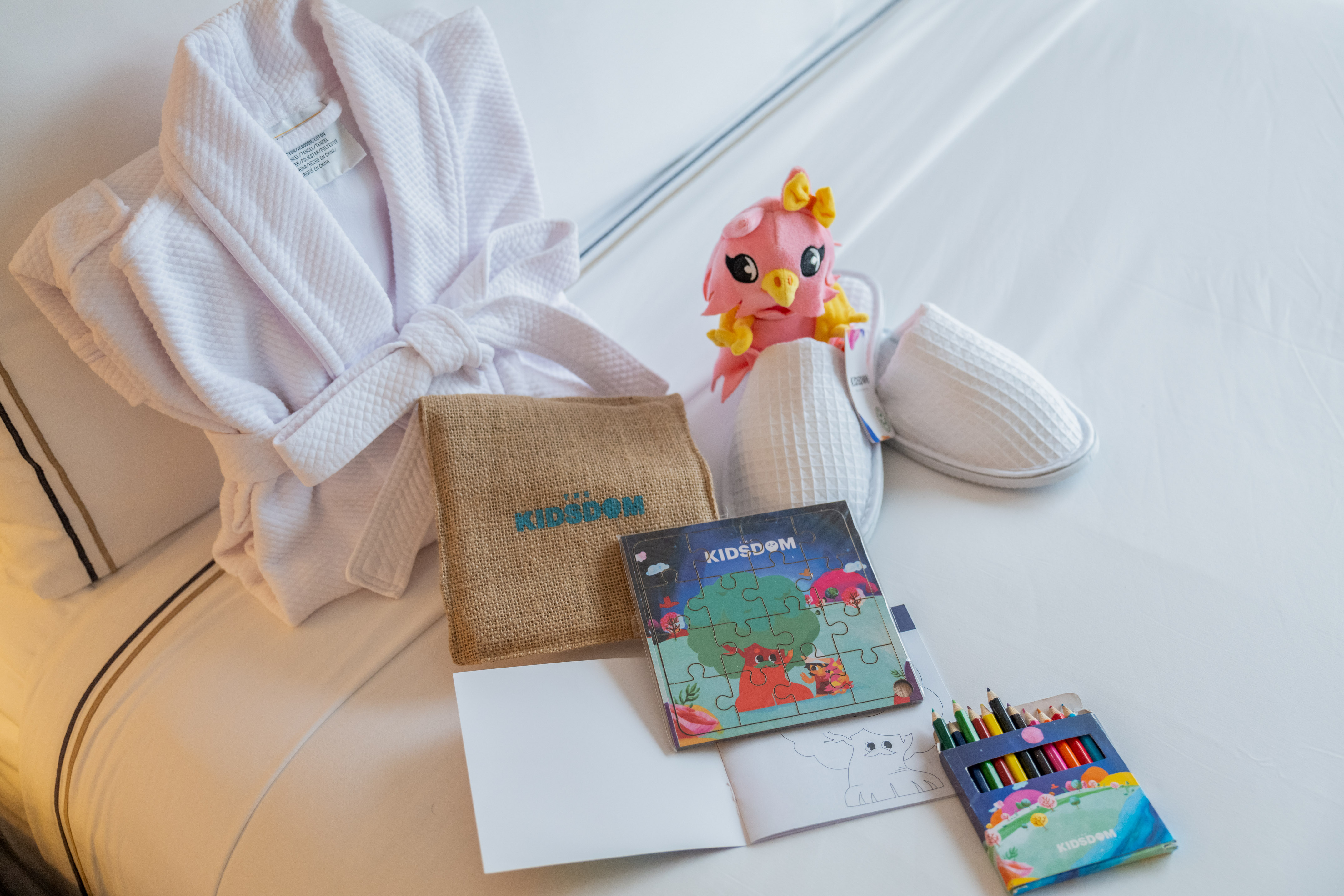 Kidsdom hotel amenities: bathrobe, slippers, plush toy, puzzle, coloring kit.