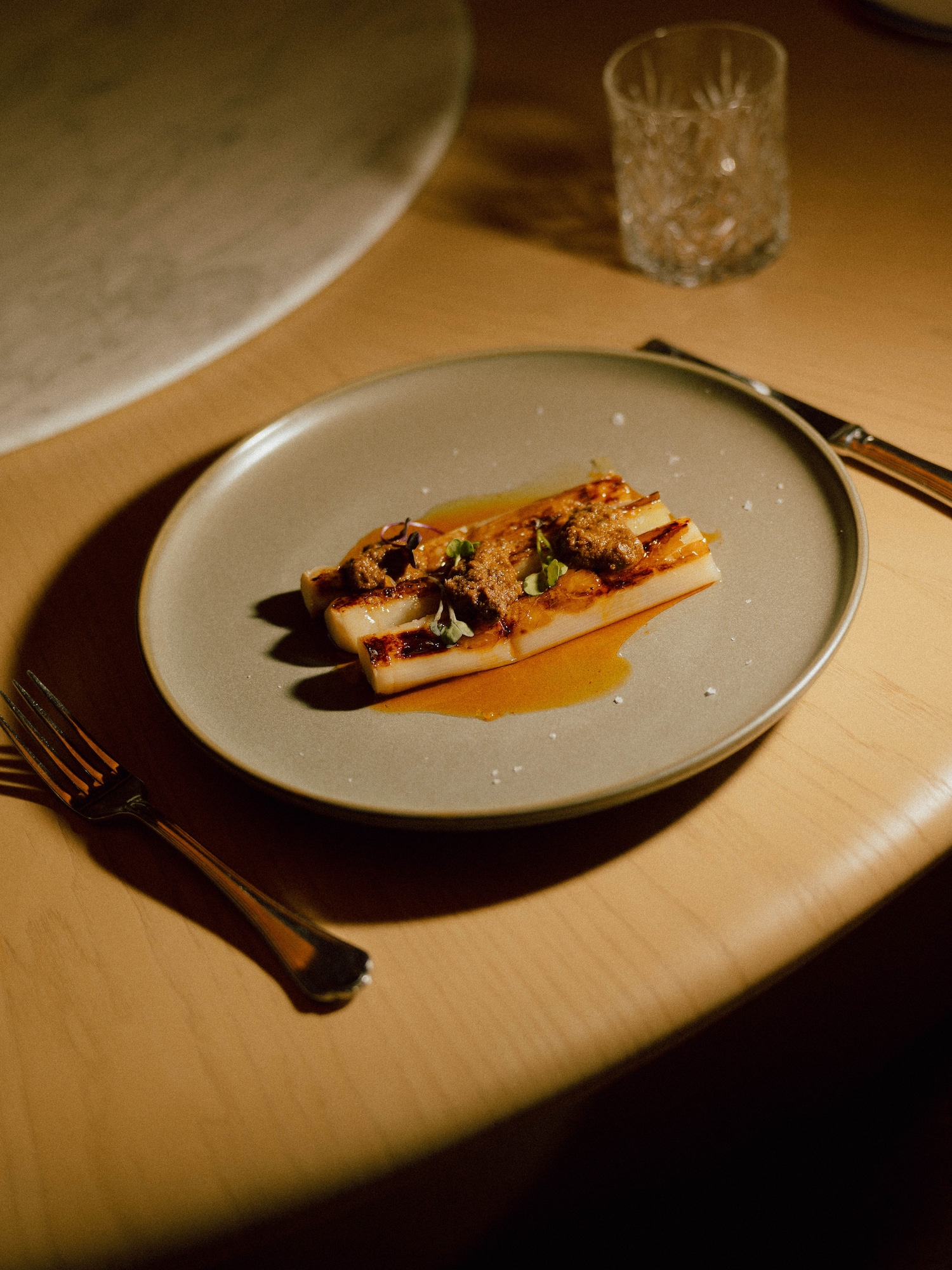 Plated caramelized white asparagus with savory topping and golden sauce.