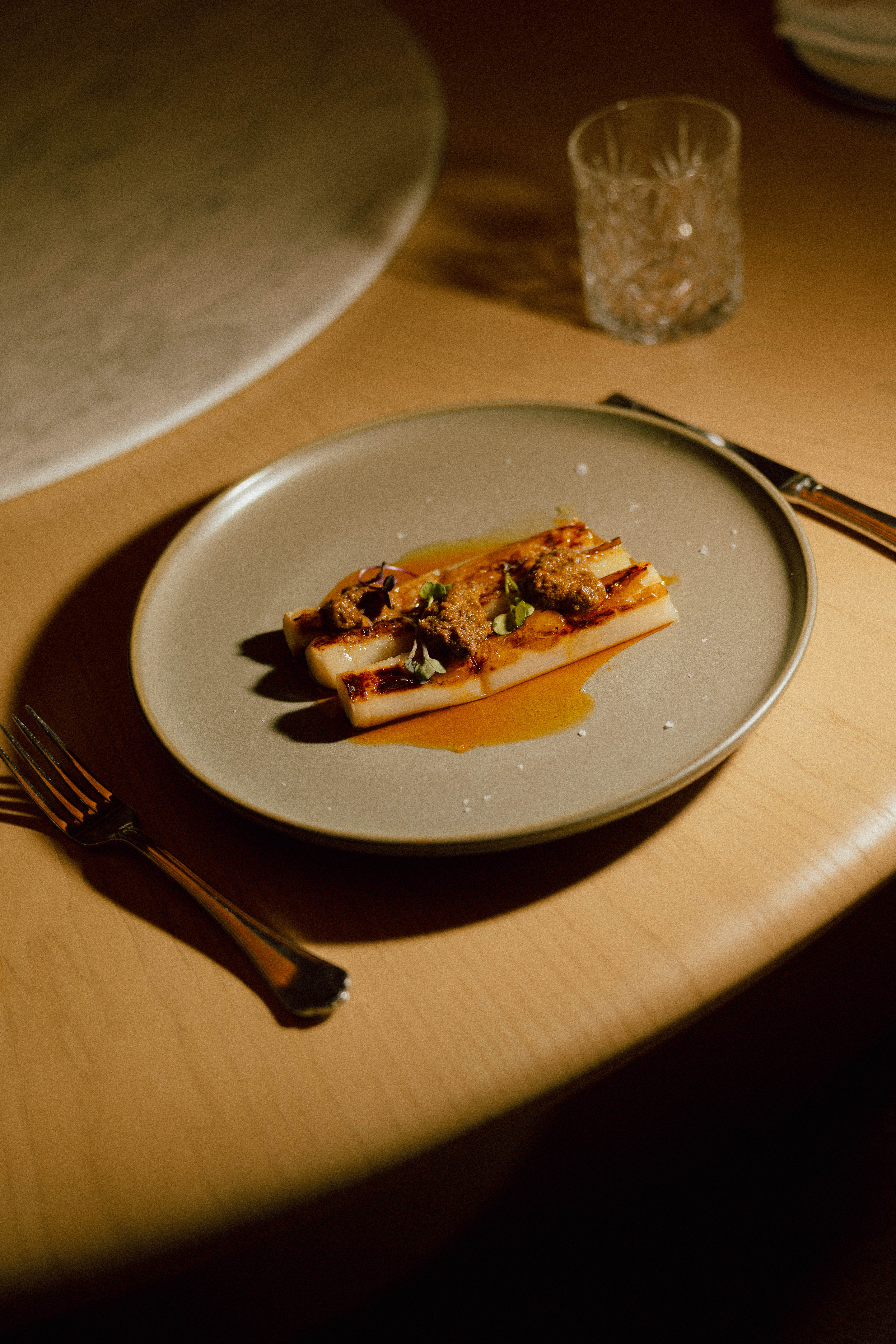 Plated caramelized white asparagus with savory topping and golden sauce.
