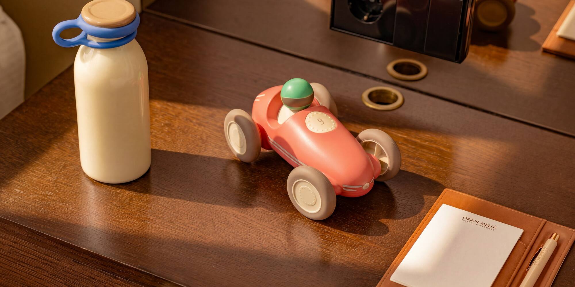 Pink toy race car, bottle, and Gran Meliá notepad on a wooden hotel desk.