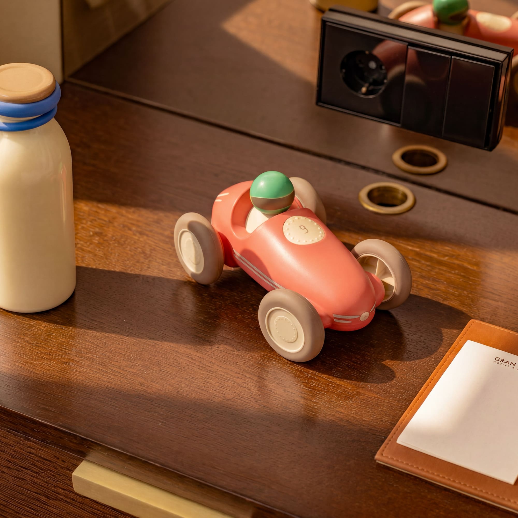 Pink toy race car, bottle, and Gran Meliá notepad on a wooden hotel desk.