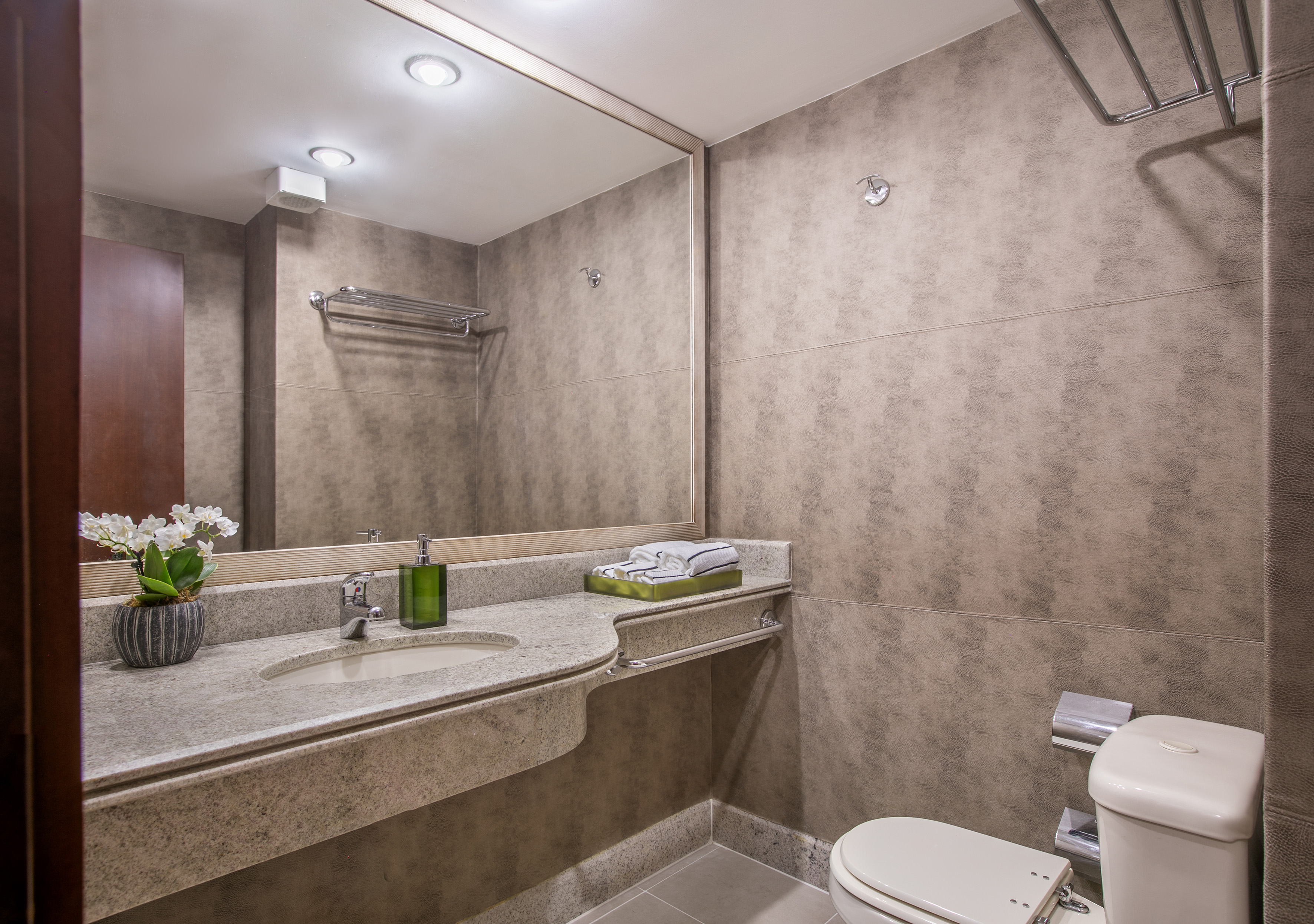 Modern hotel bathroom with granite vanity, sink, mirror, and toilet.