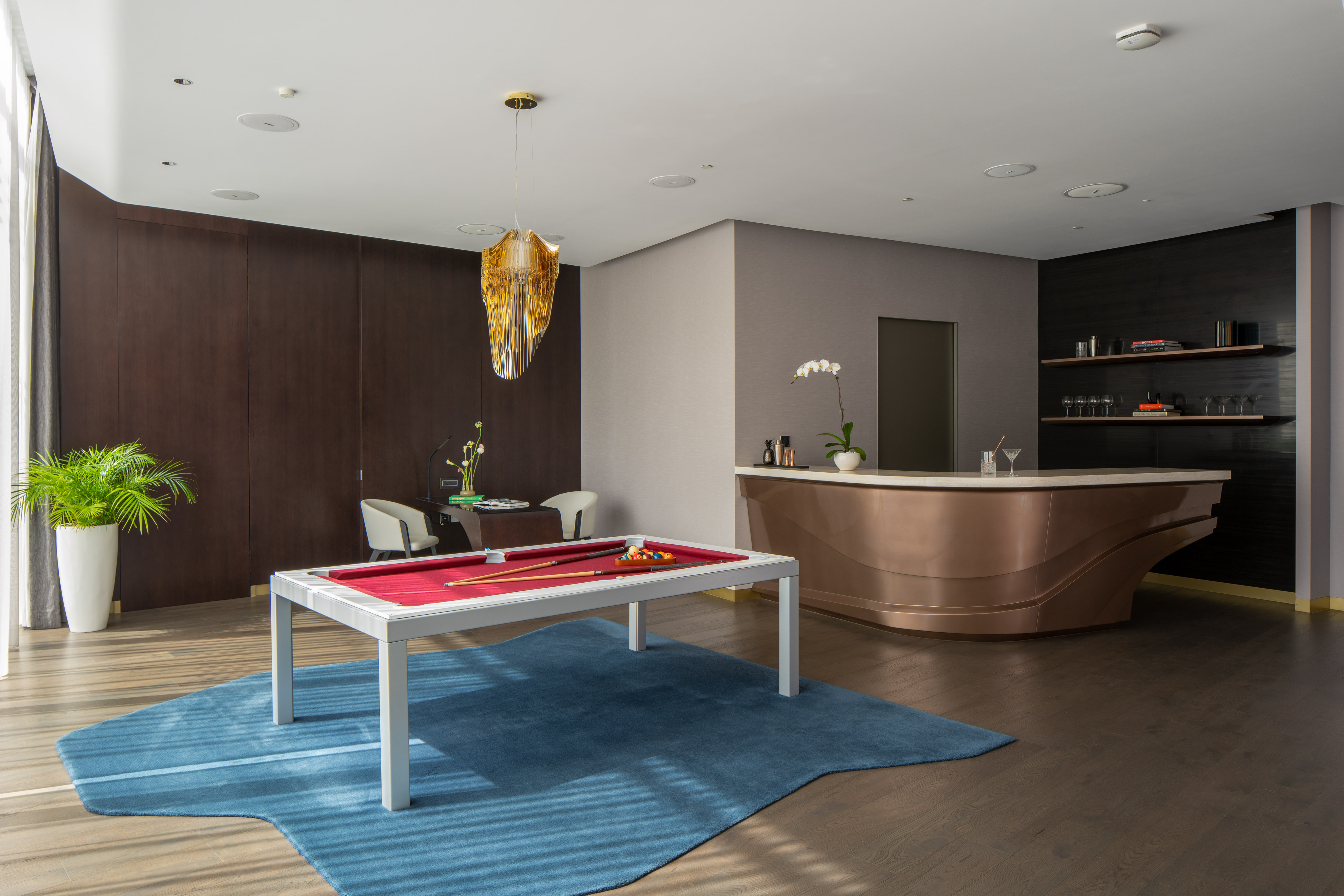 Modern game room with white billiard table, blue rug, and curved copper bar.