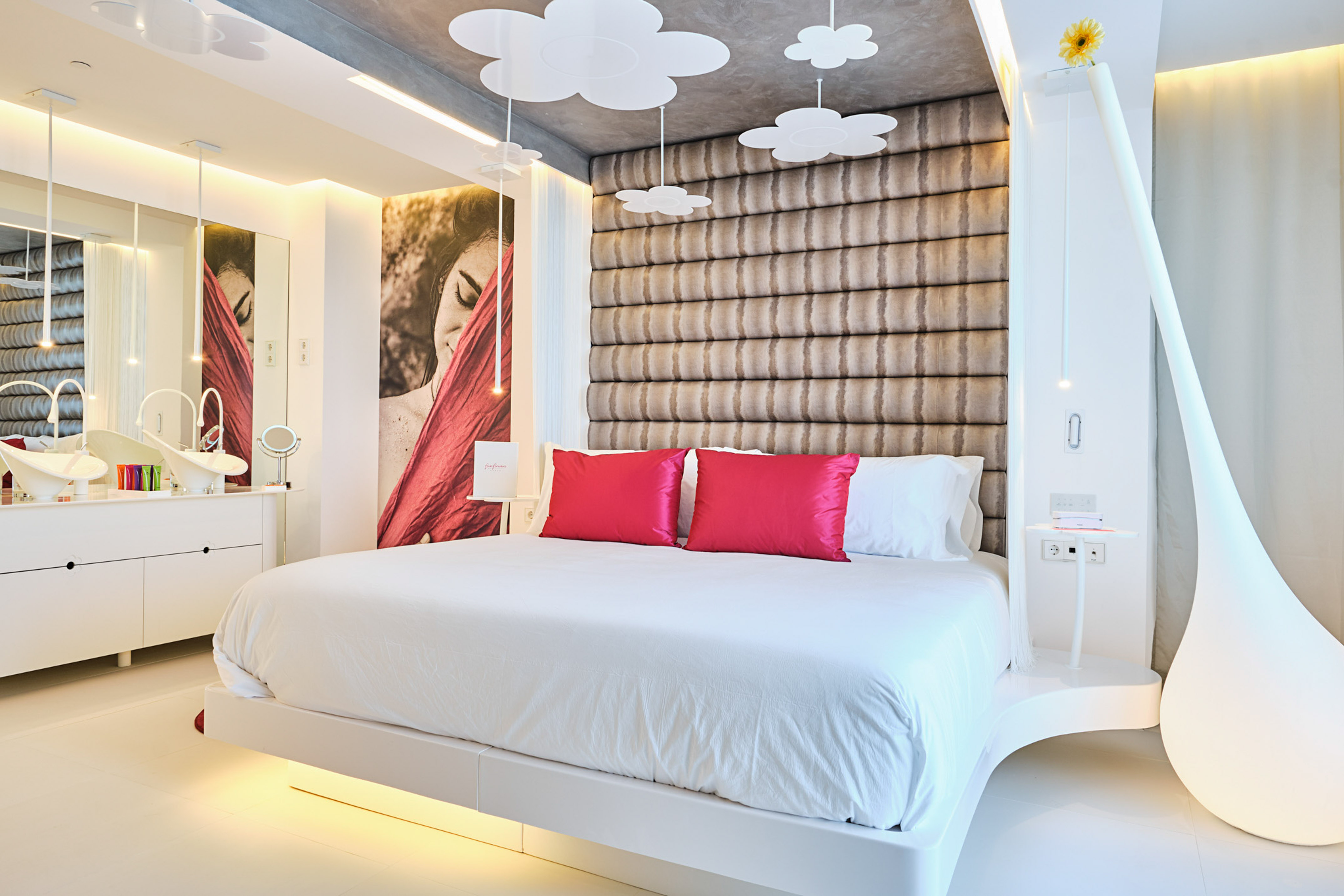 Contemporary hotel room with white bed, pink pillows, cloud lighting, and vanity.