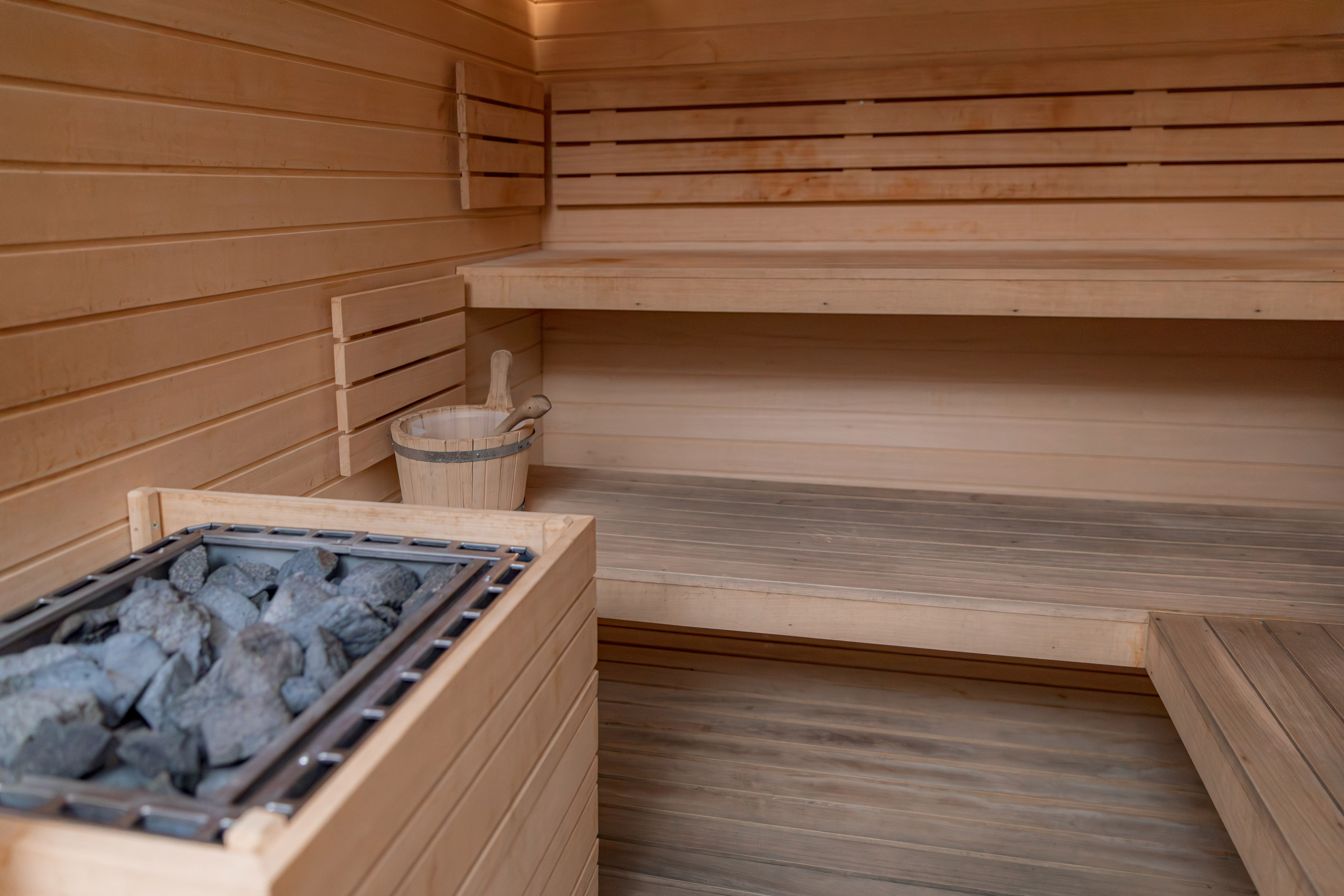 Wooden sauna interior with heater, stones, bench, and bucket.