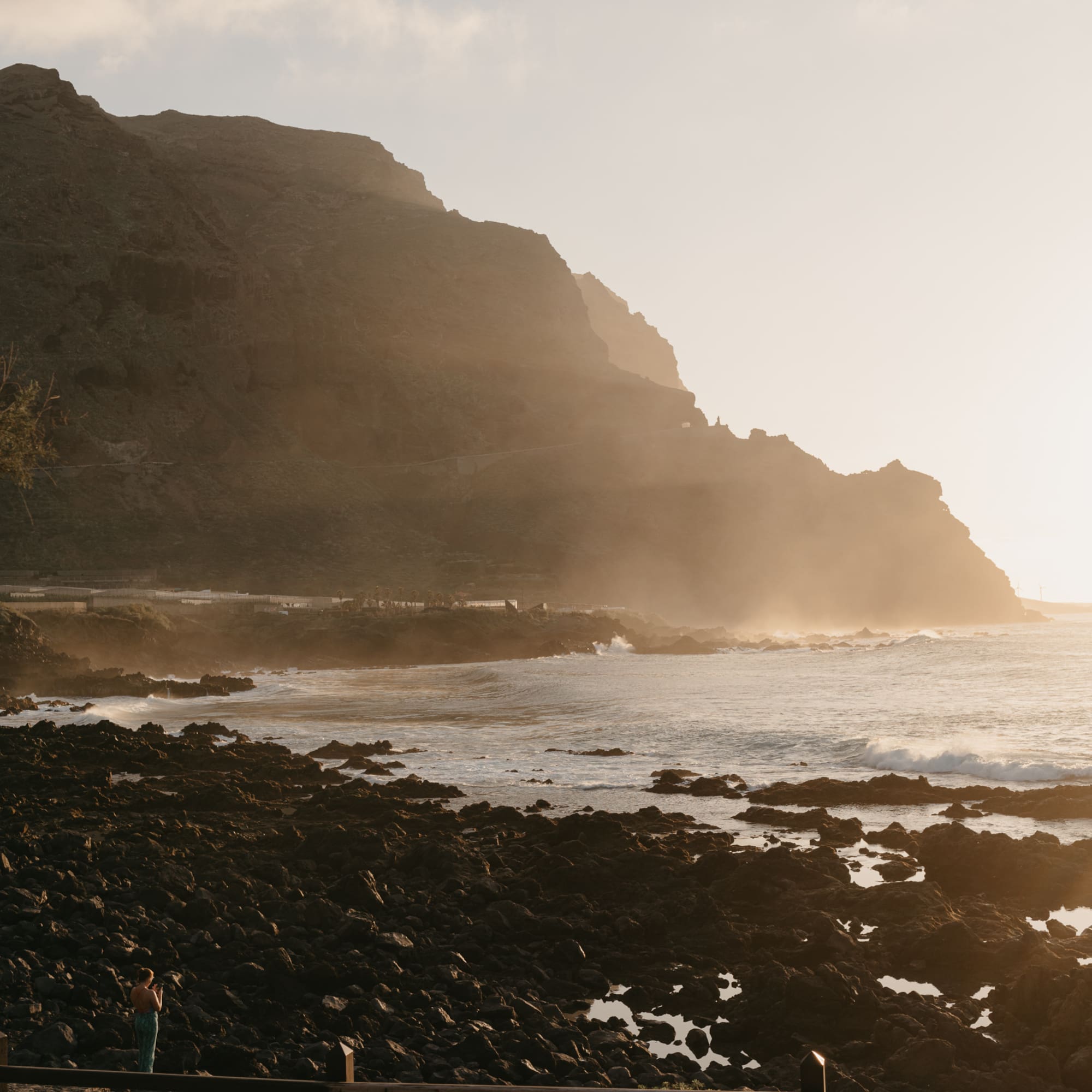 Golden sunset over rocky coast, ocean waves, and large cliffs.