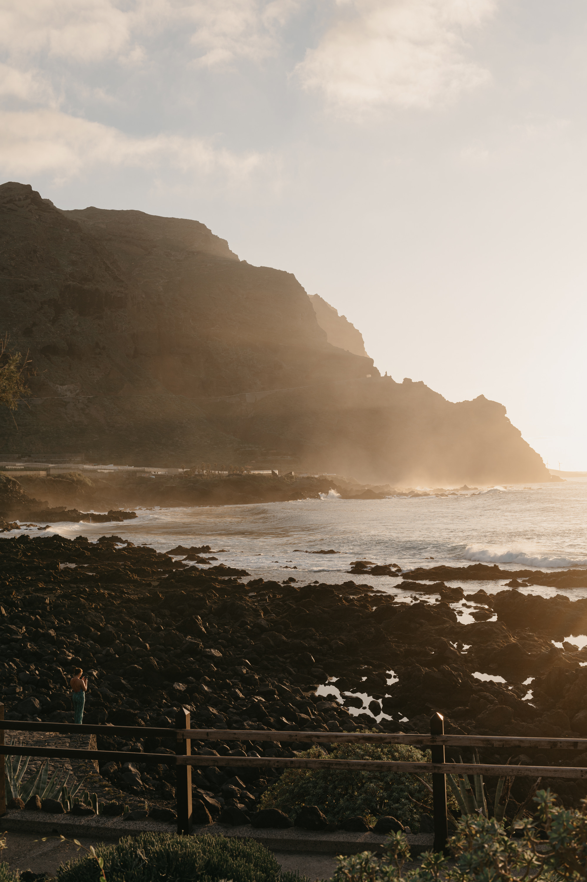 Golden sunset over rocky coast, ocean waves, and large cliffs.