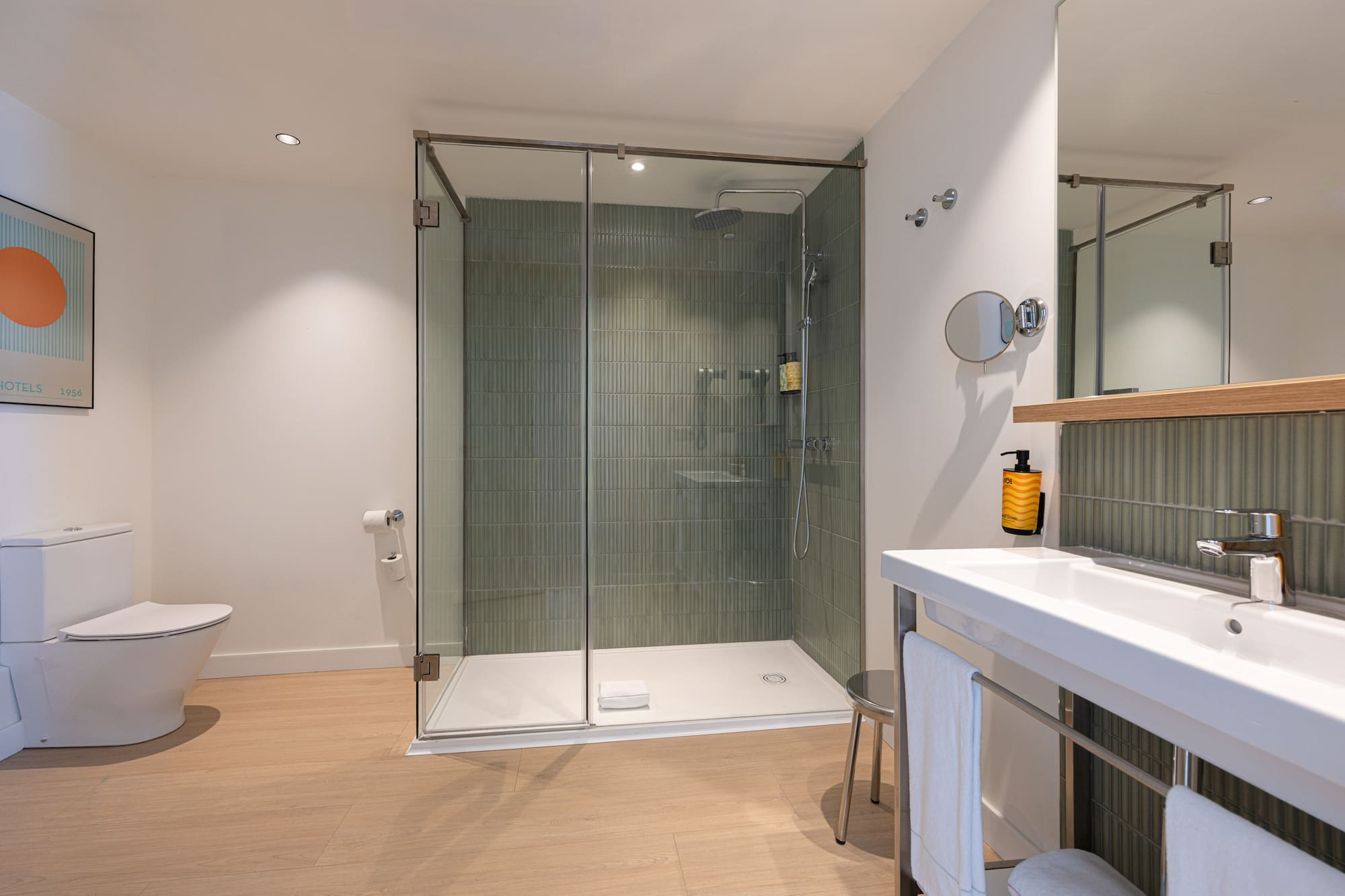 Modern bathroom with walk-in glass shower, green tiles, toilet, and sink.