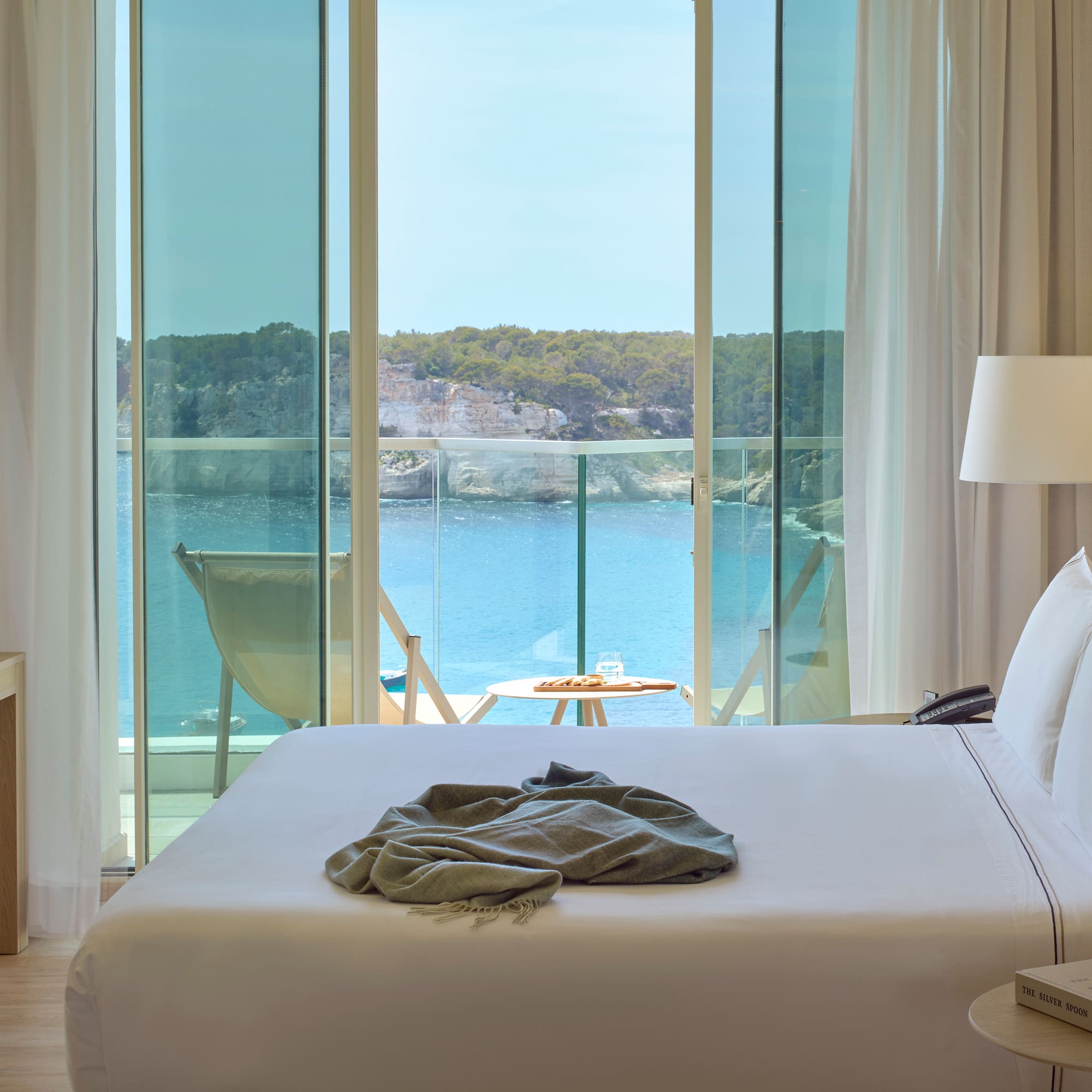 a bed with a blanket on it and a table with chairs and a table with a lamp and a table with a chair and a table with a table and a chair with a table and a chair