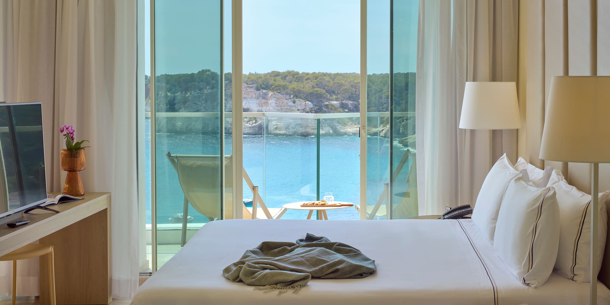 a bed with a blanket on it and a table with chairs and a table with a lamp and a table with a chair and a table with a table and a chair with a table and a chair