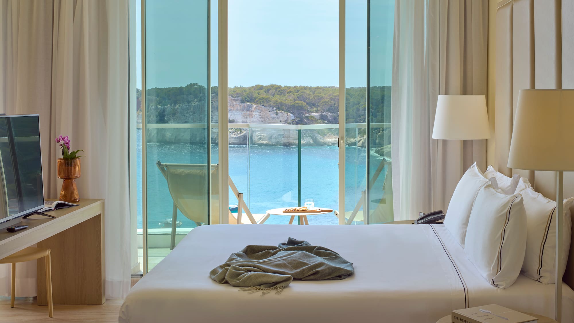 a bed with a blanket on it and a table with chairs and a table with a lamp and a table with a chair and a table with a table and a chair with a table and a chair