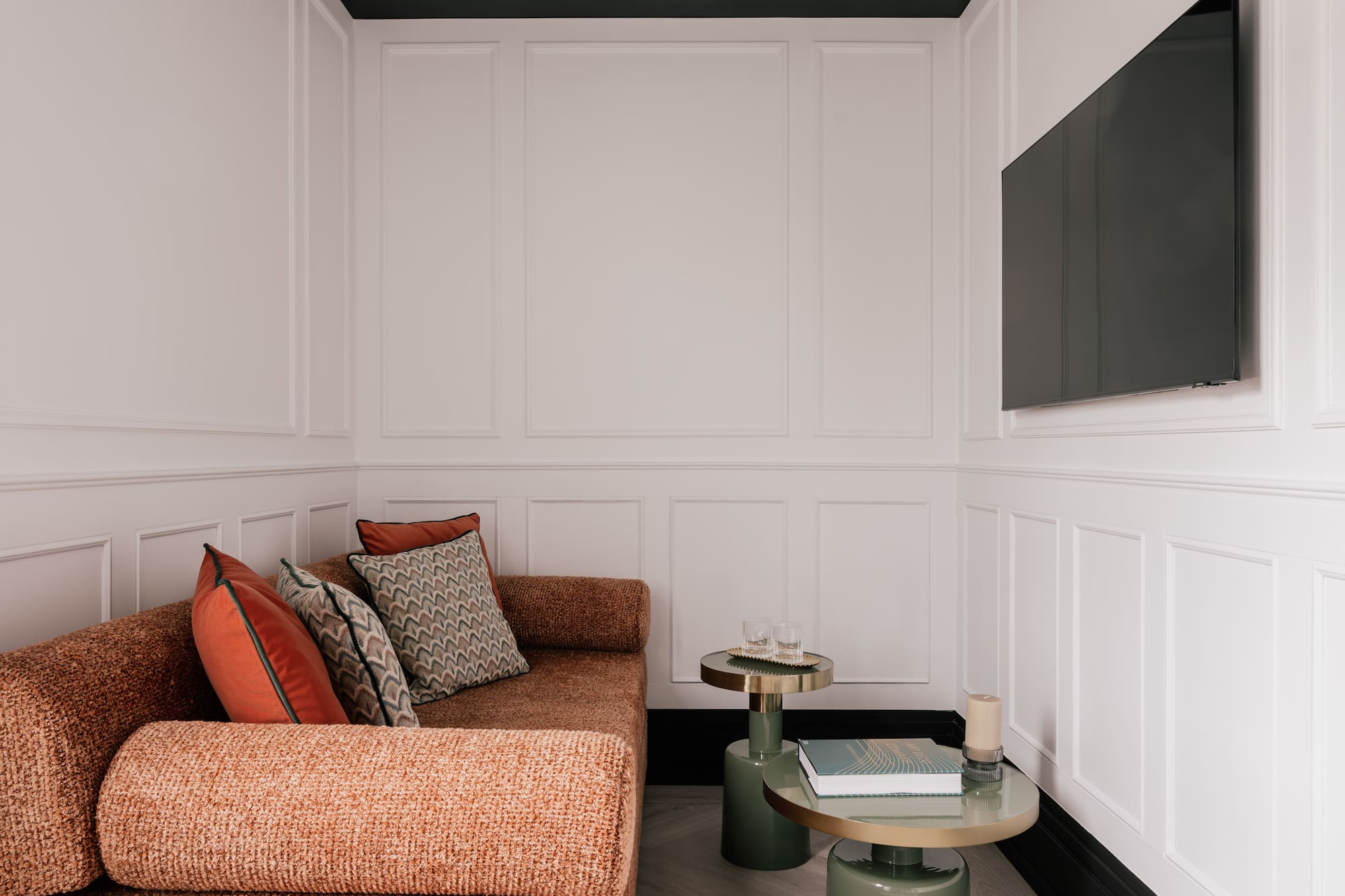 Modern living room with rust sofa, white paneled walls, TV, and accent tables.
