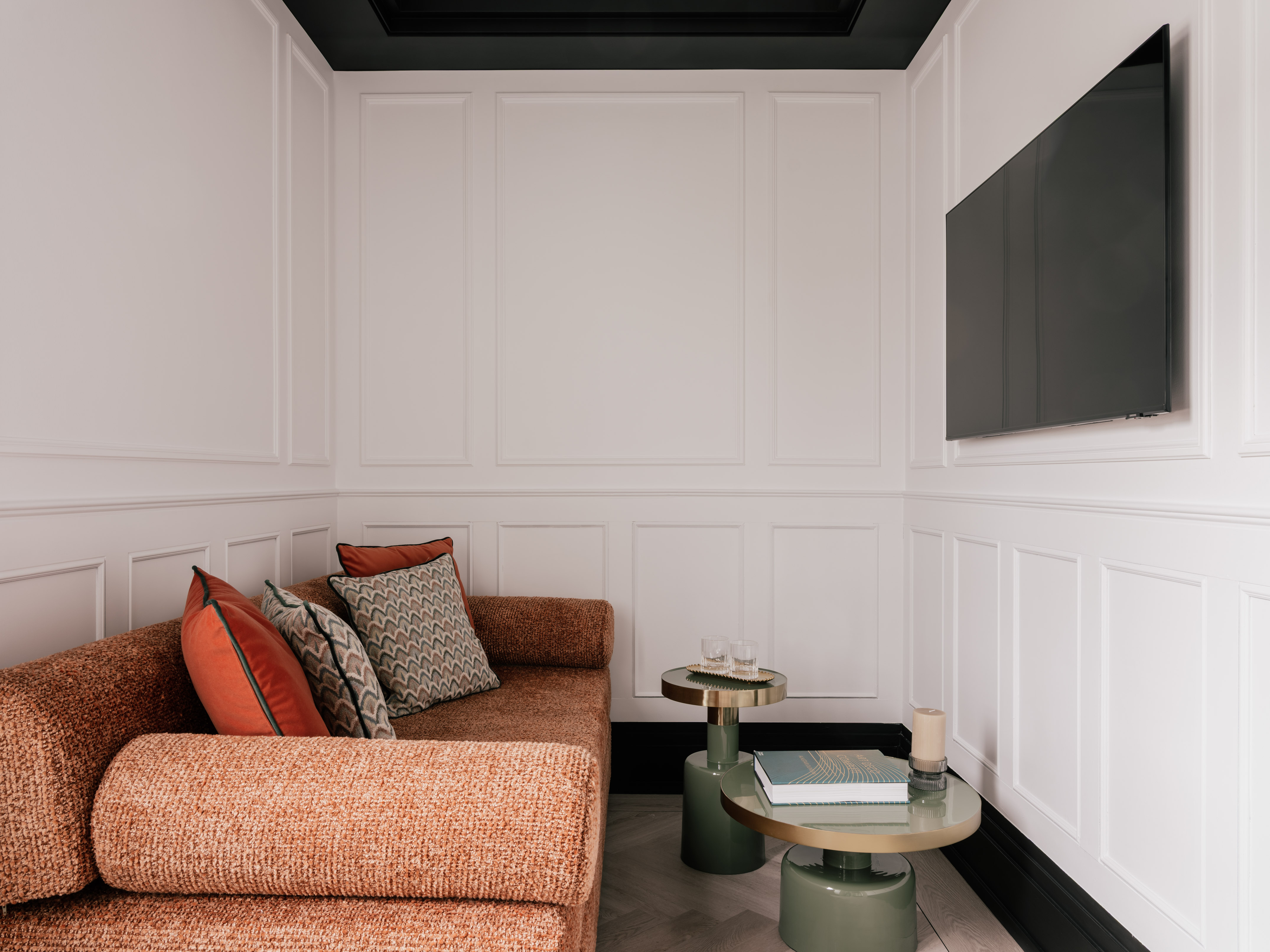 Modern living room with rust sofa, white paneled walls, TV, and accent tables.