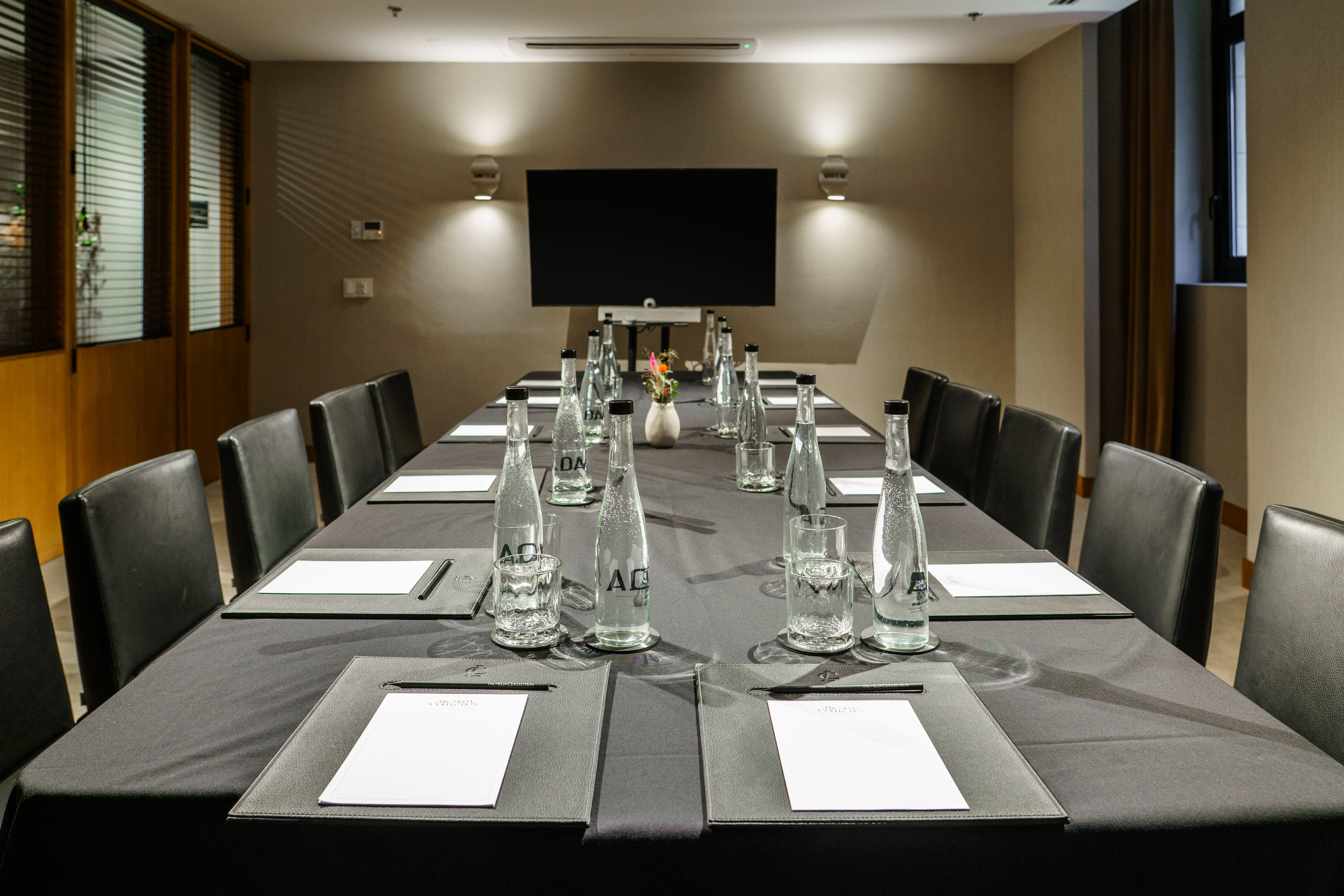 Modern conference room with black table, leather chairs, water bottles, and display.