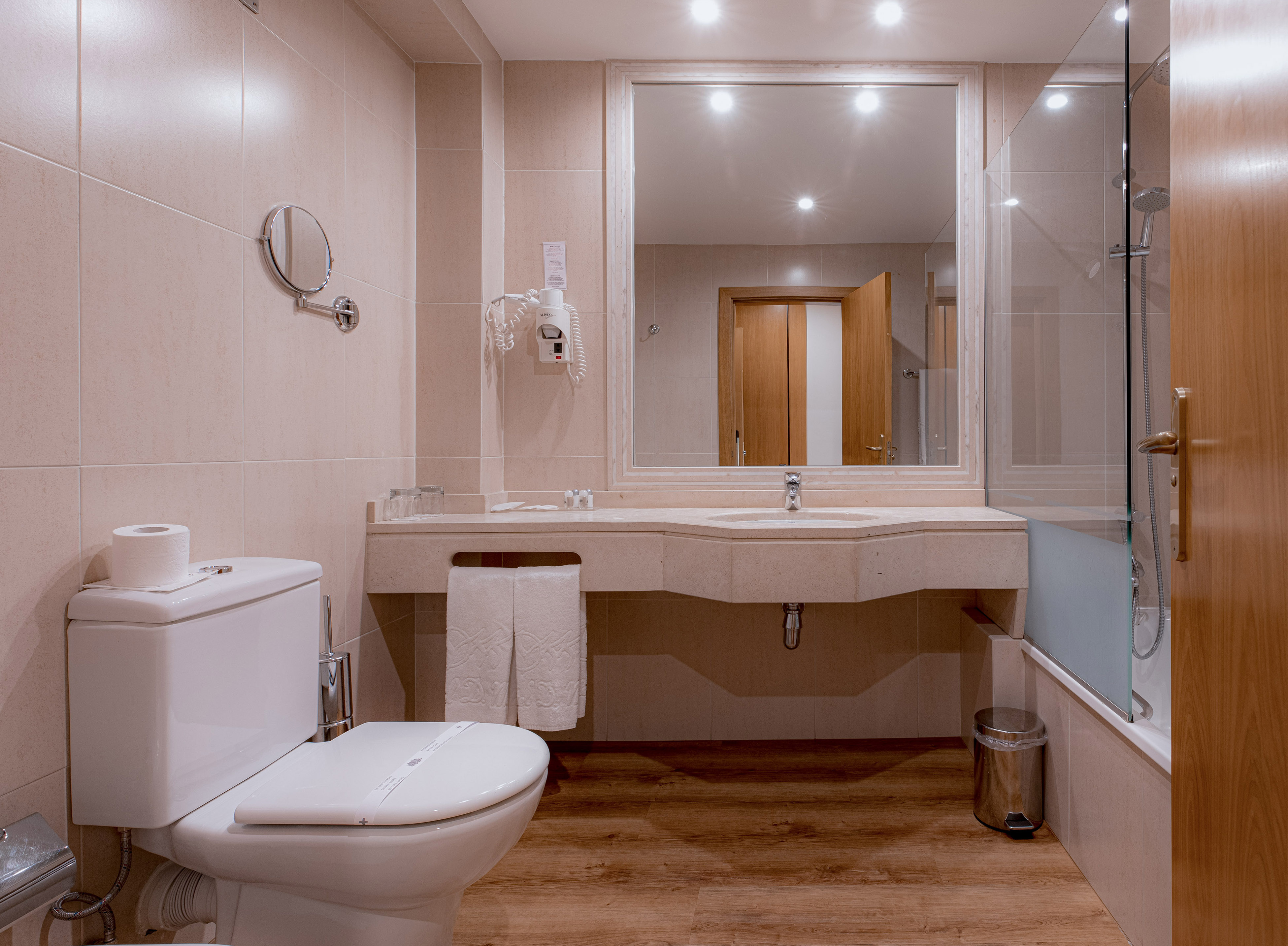Modern hotel bathroom with toilet, vanity, sink, large mirror, and shower.