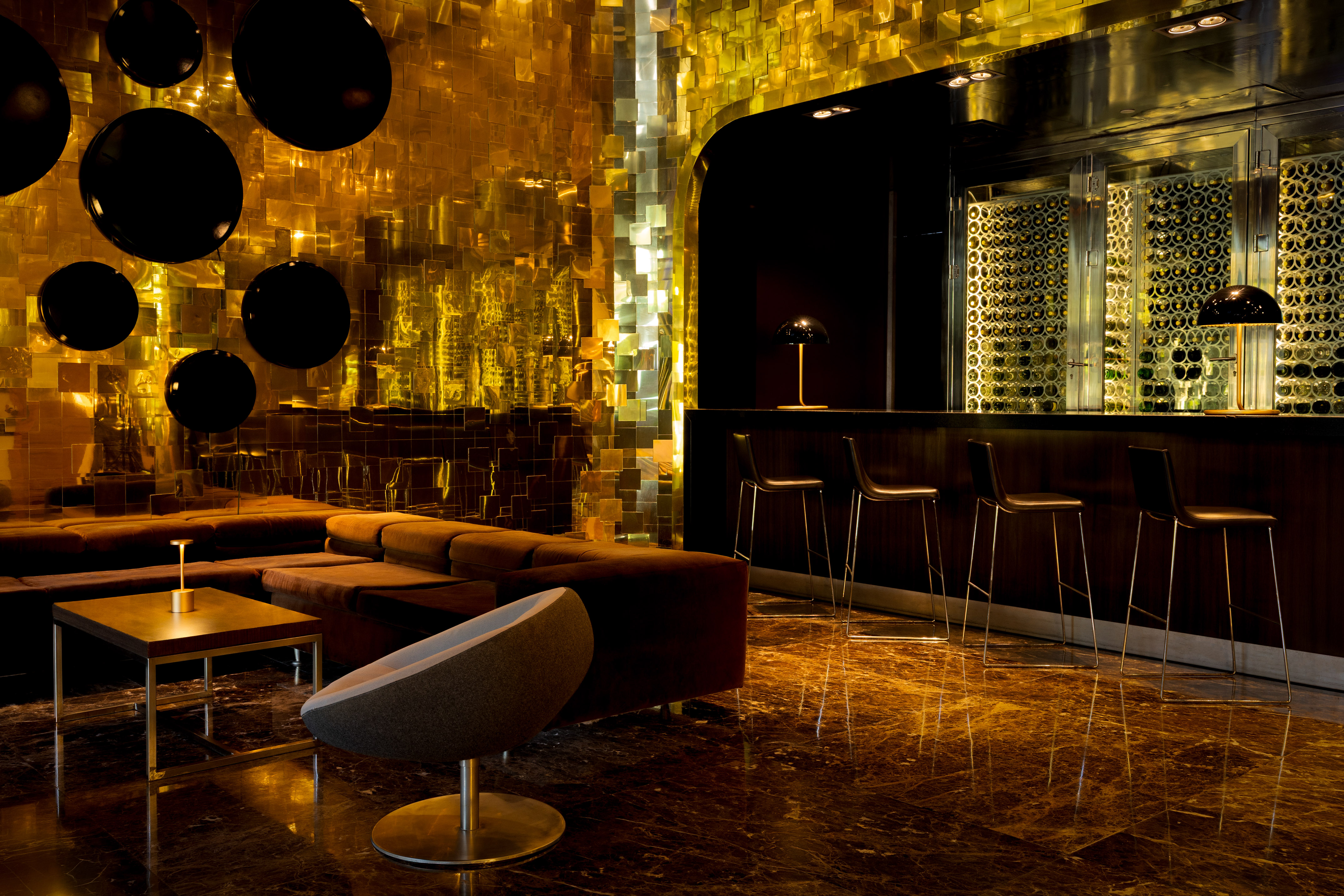 Luxury bar lounge with golden walls, wine display, and modern seating.