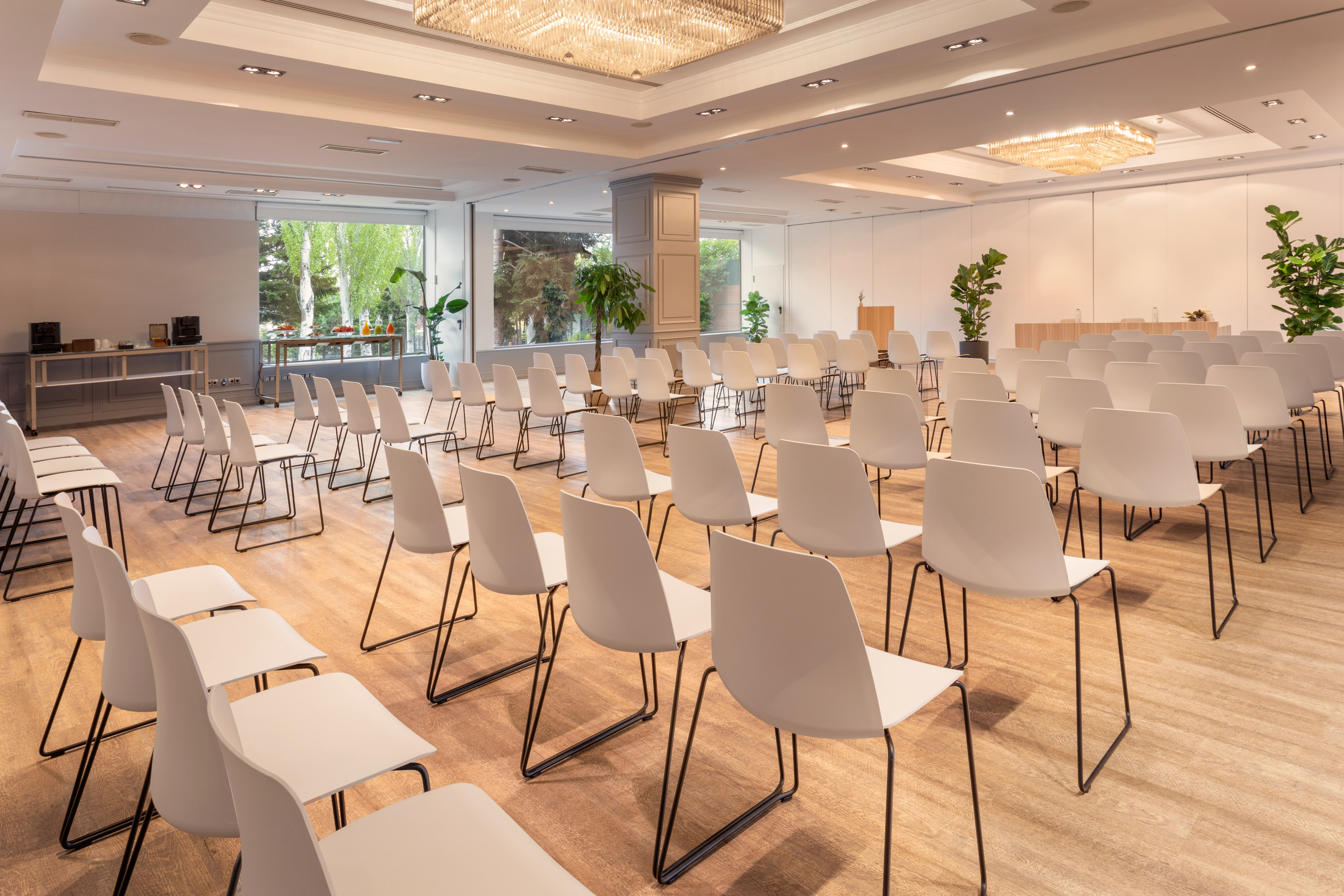 Modern hotel meeting room with white chairs, large windows, and beverage station.