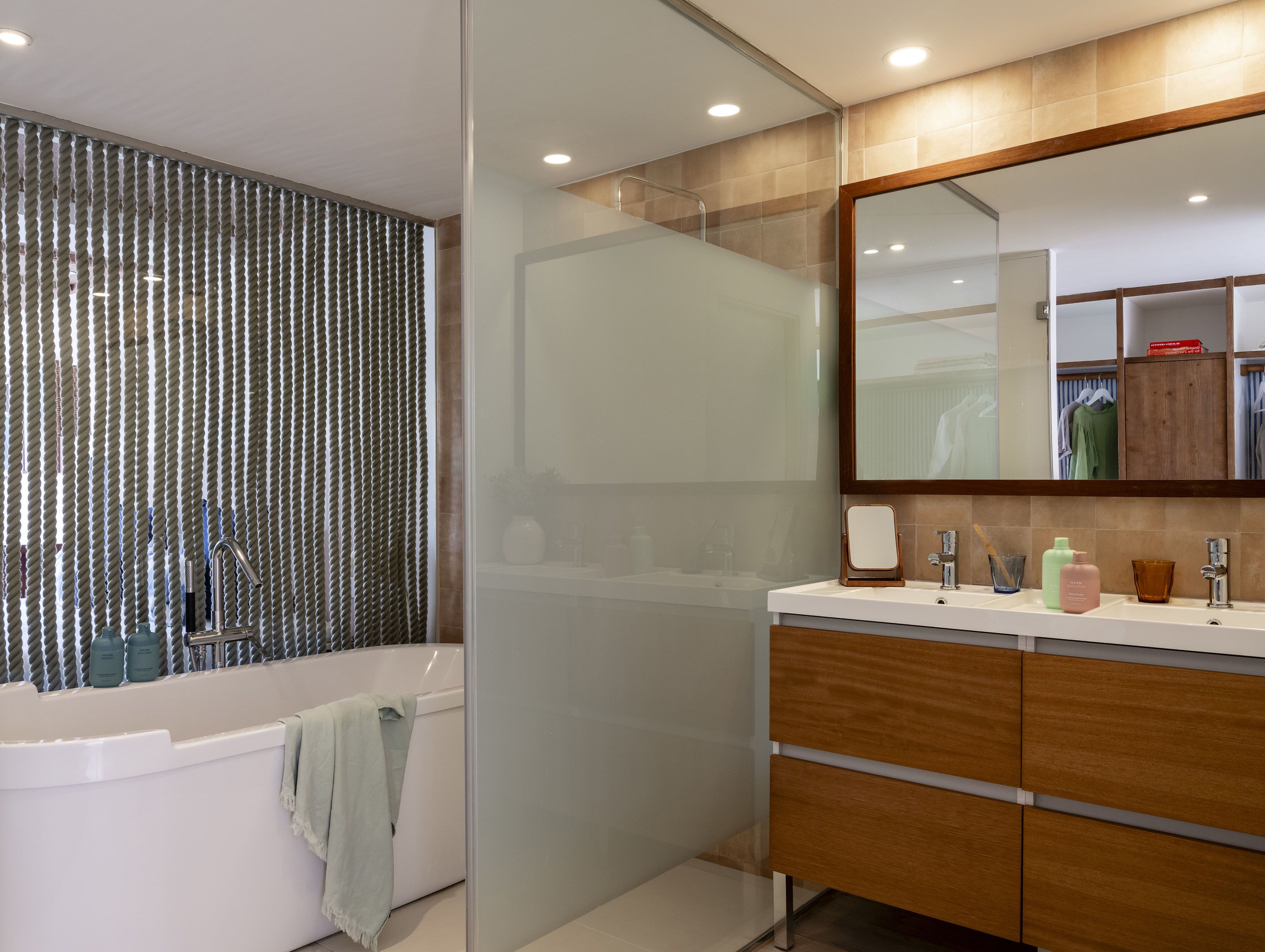 Modern bathroom with white tub, wood vanity, rope wall, and glass shower.