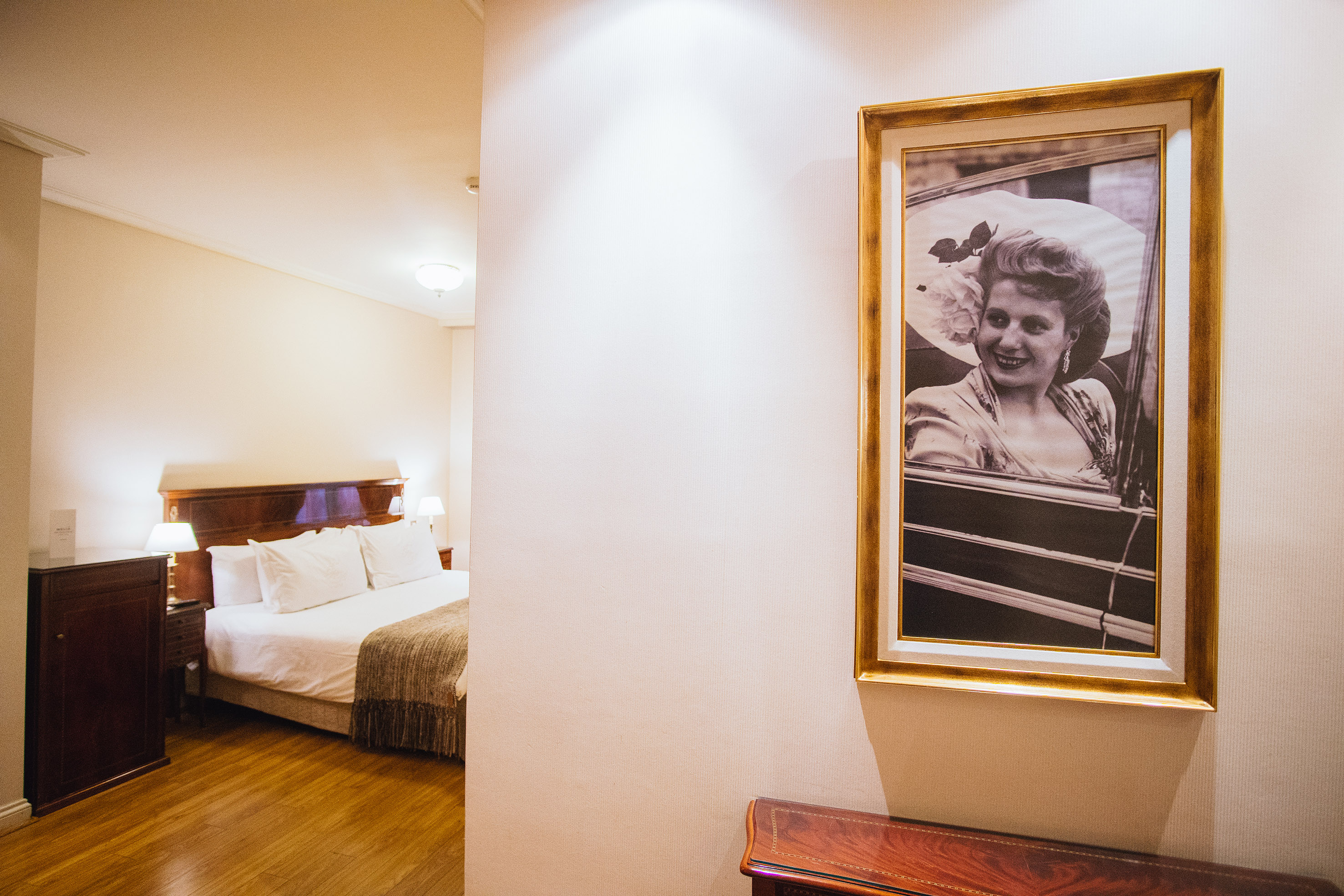 Hotel bedroom with framed vintage portrait of woman and wooden bed.