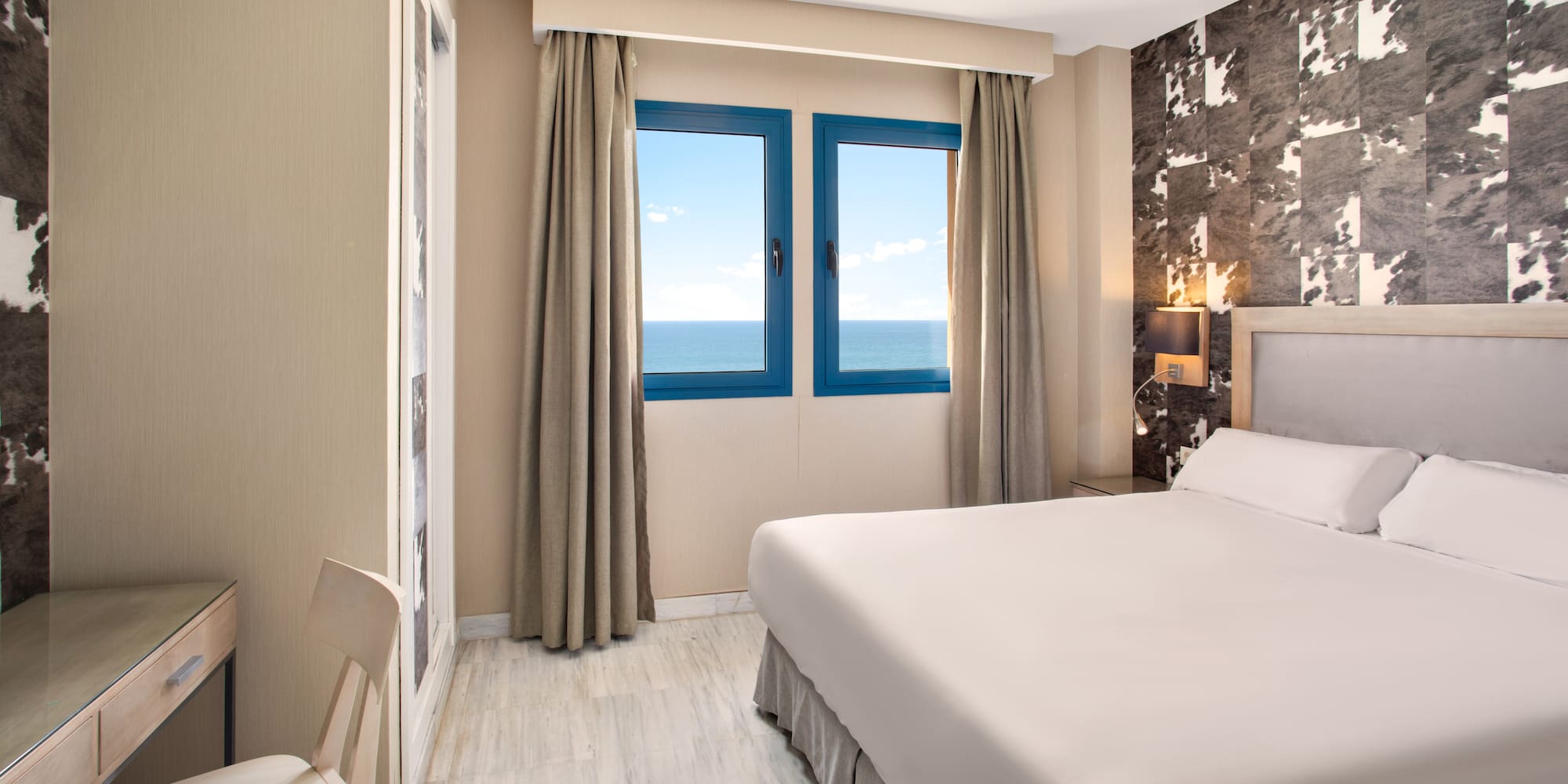 Modern hotel bedroom with sea view, large bed, and desk.